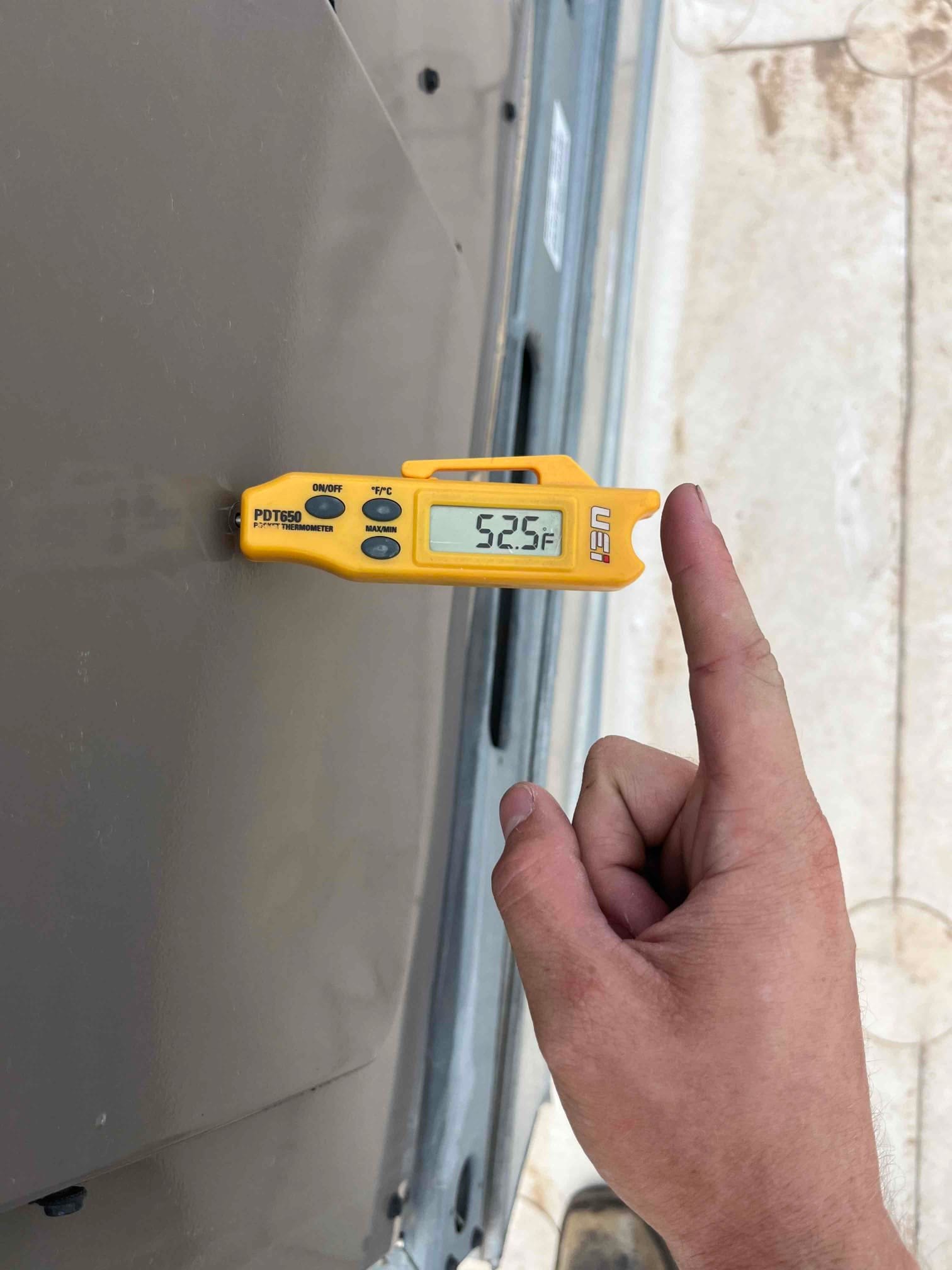 Digital thermometer shows 52.5 °F surface temperature on the HVAC unit cabinet during air conditioning repair.