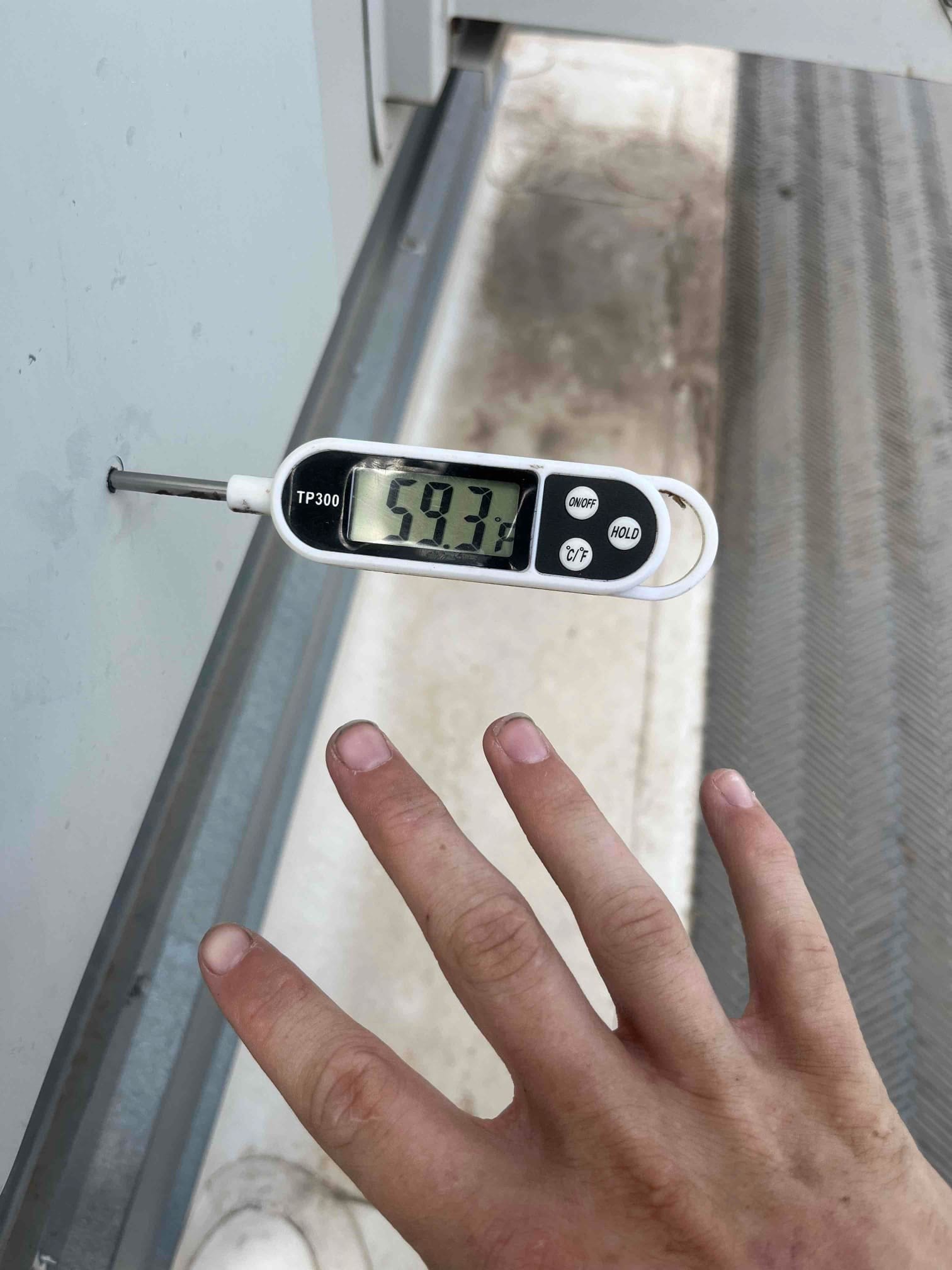 Digital thermometer shows 59.3 °F surface temperature at the repair site during air conditioning repair.