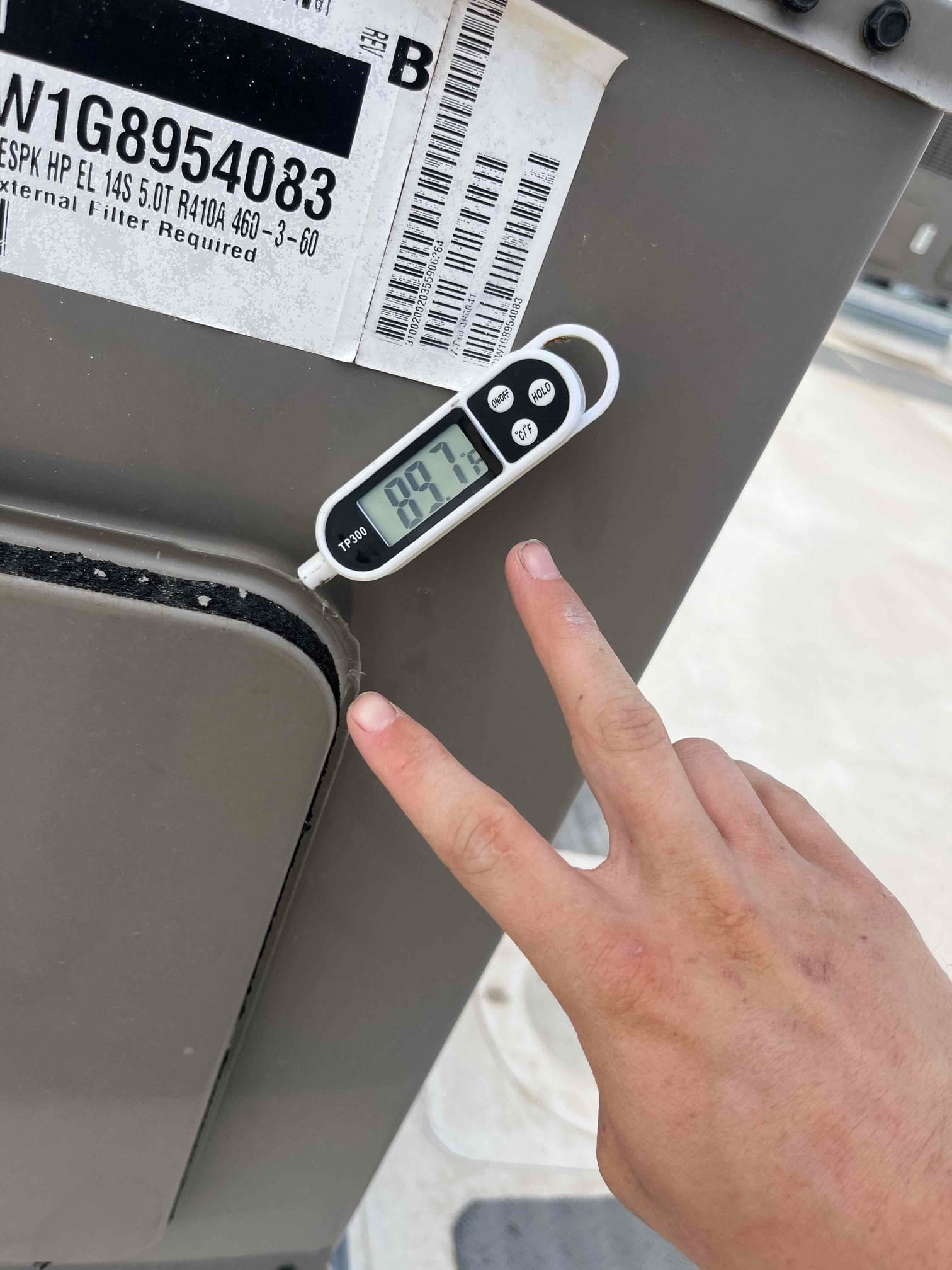 Digital thermometer shows 99.7 °F on the metal panel of the outdoor air conditioning unit cabinet.
