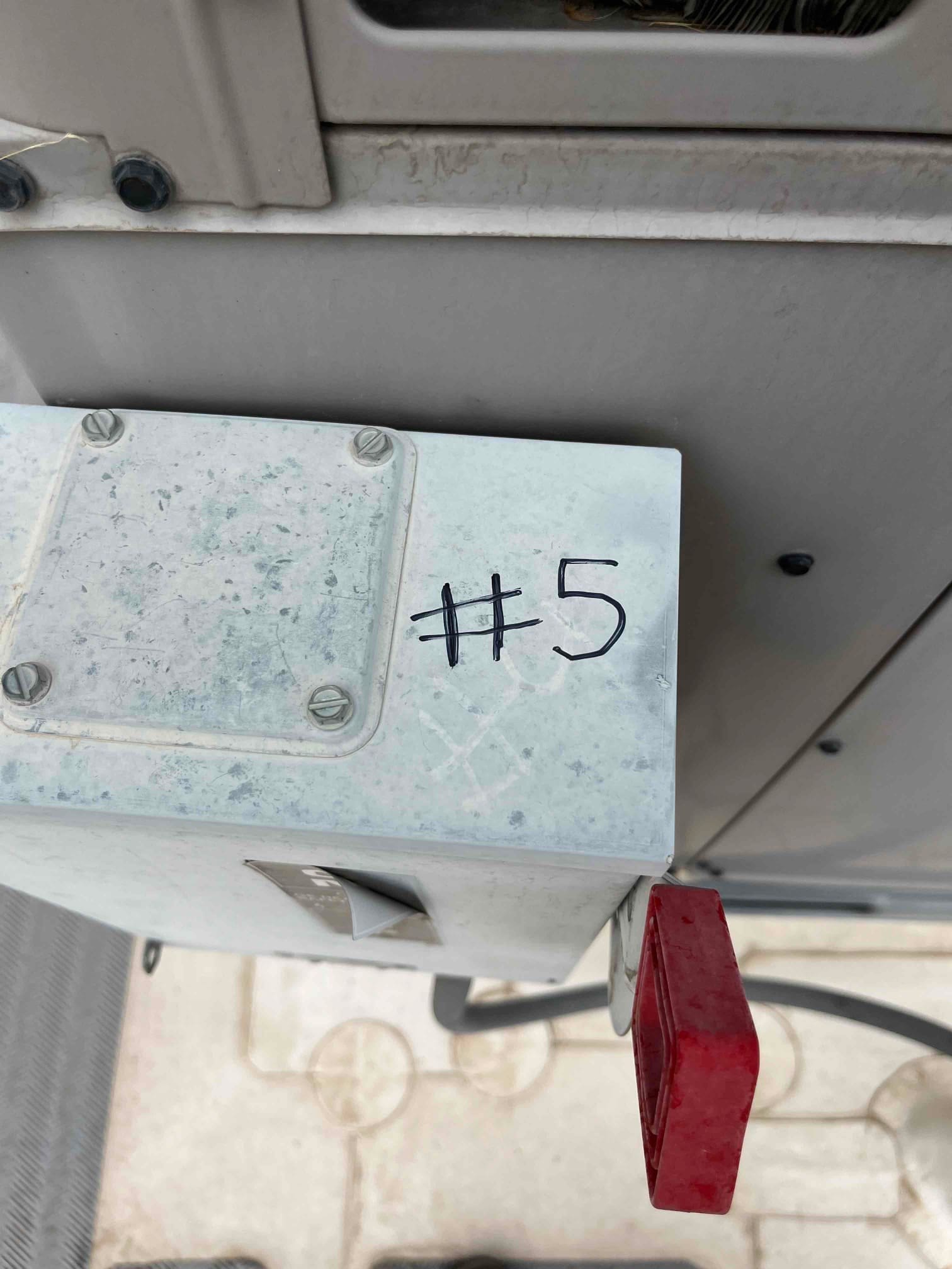 Outdoor electrical disconnect enclosure labeled #5 next to the air conditioning unit, showing closed cover and red handle.