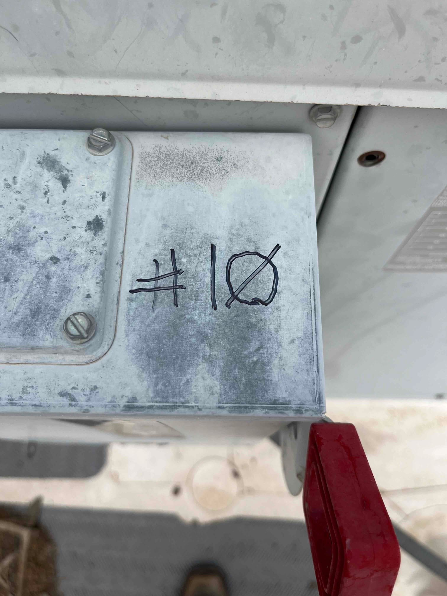 Outdoor electrical enclosure with hand-marked label “#10” next to a red-handled disconnect switch on the HVAC unit.