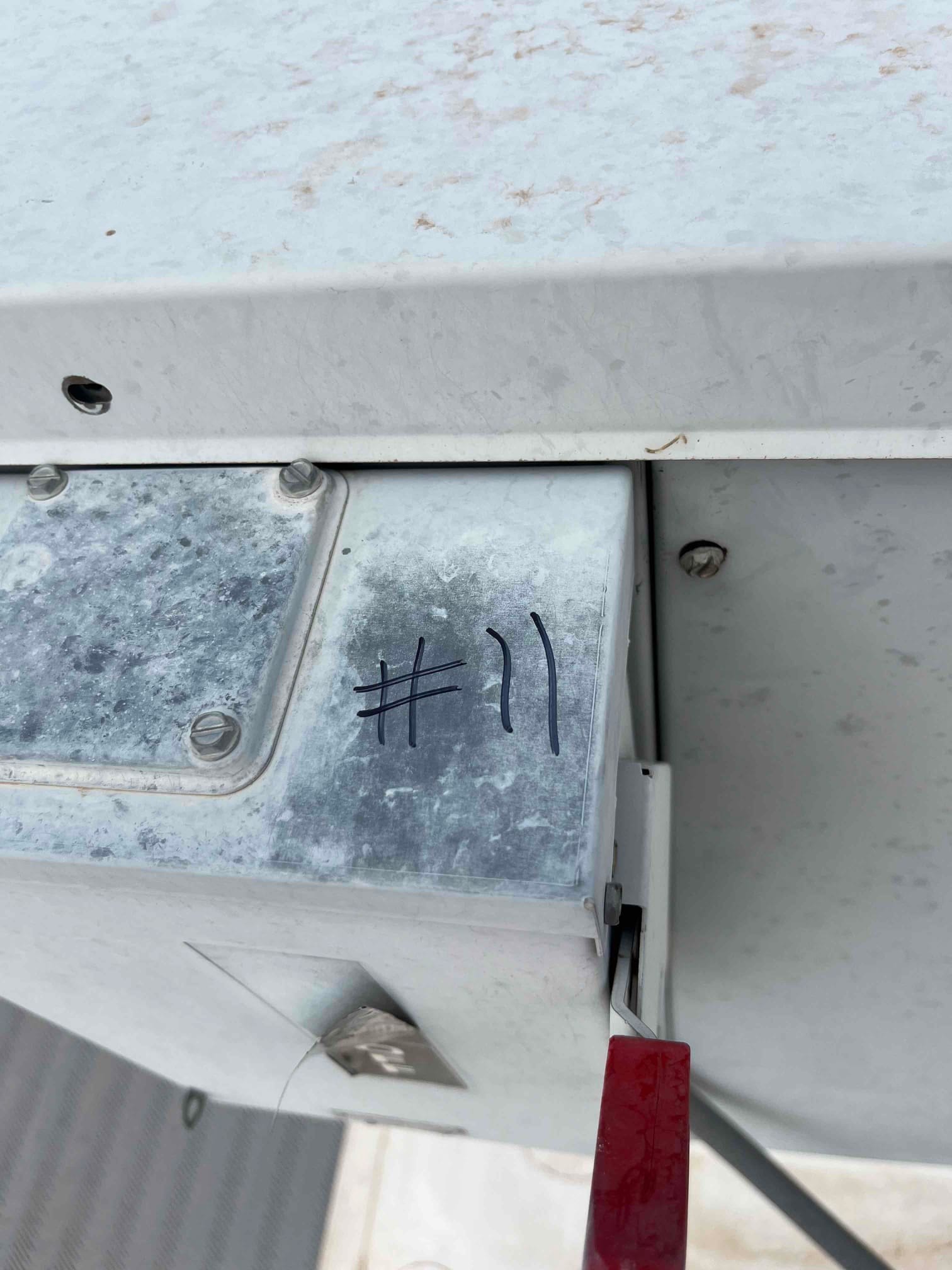 Outdoor electrical junction box near HVAC equipment, labeled with marker as number 11, showing weathered metal housing and fasteners.