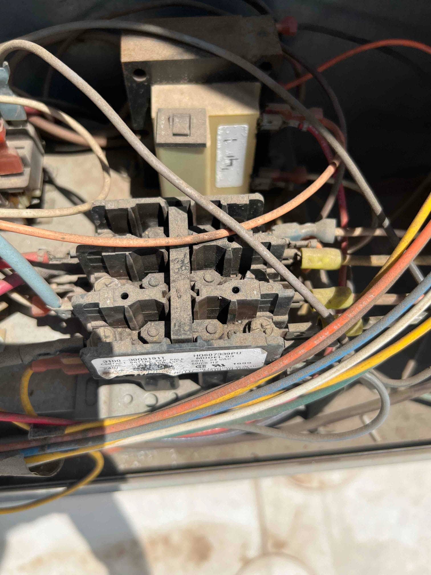Surface-mount transformer and contactor wiring inside the condenser compartment, showing multiple connected conductors and dusty components.