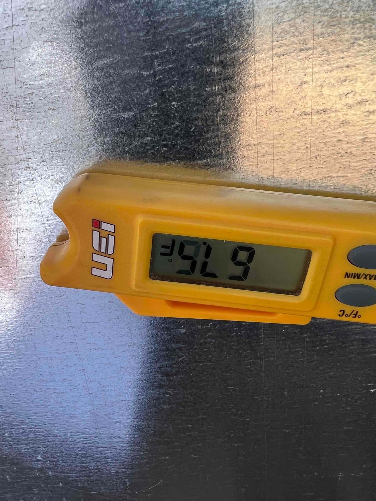 Digital thermometer on metal duct shows 55 degrees Fahrenheit, documenting cold supply air leaving the evaporator.