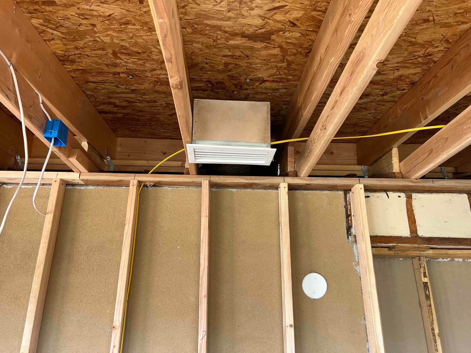 Framed ceiling area showing a newly installed return grille and duct box routed between joists during HVAC installation.