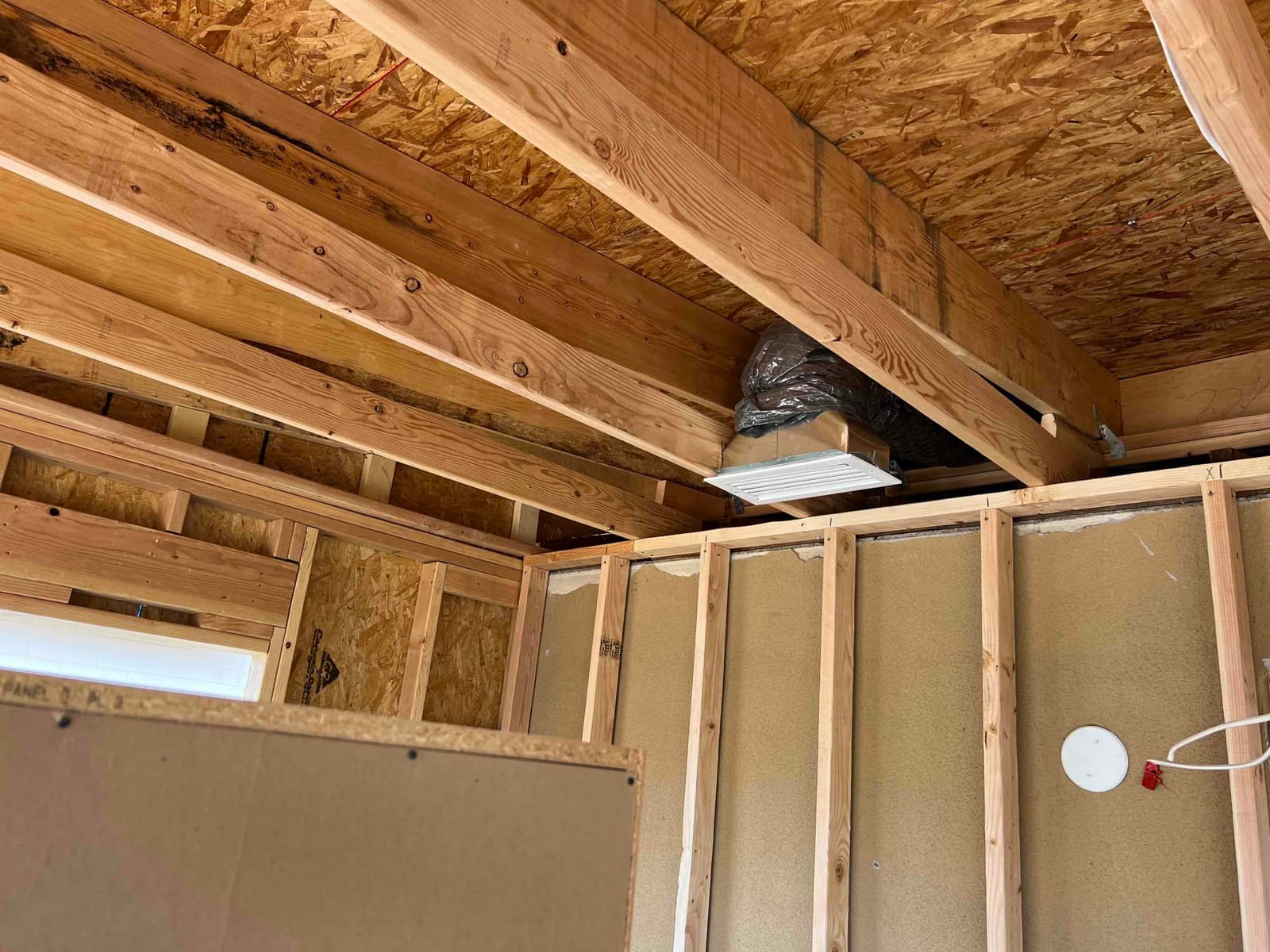 Framed interior with insulated flexible duct and ceiling supply register box installed between joists during HVAC rough-in.