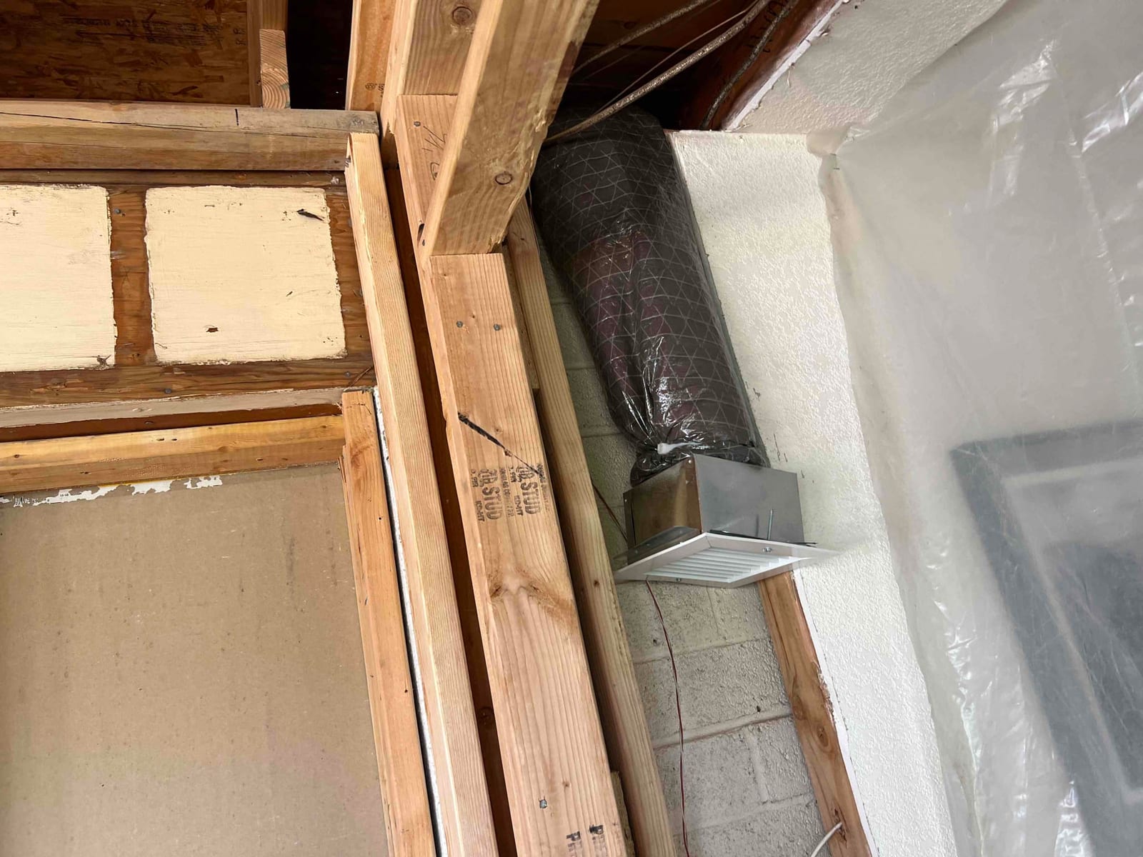 New flexible duct connected to a metal boot with a ceiling register, installed within framed wall construction.