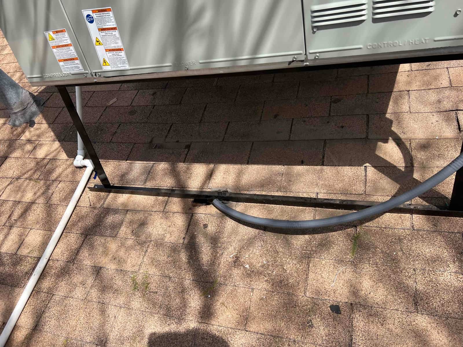 Package HVAC unit set on rooftop stand with insulated refrigerant line and PVC condensate drain routed along the roof surface.
