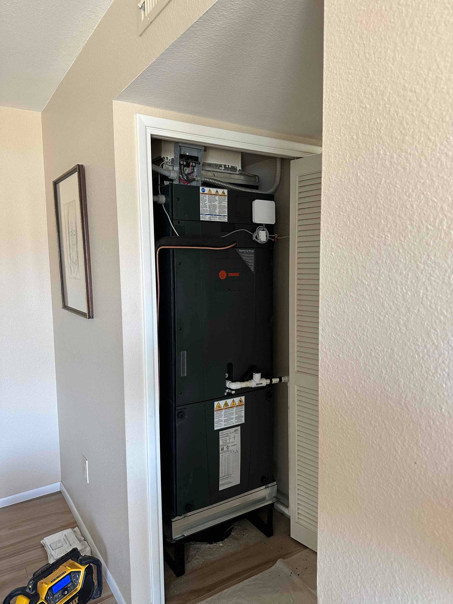 Air handler installed in a closet on a raised stand with insulated refrigerant lines and PVC condensate drain connected.
