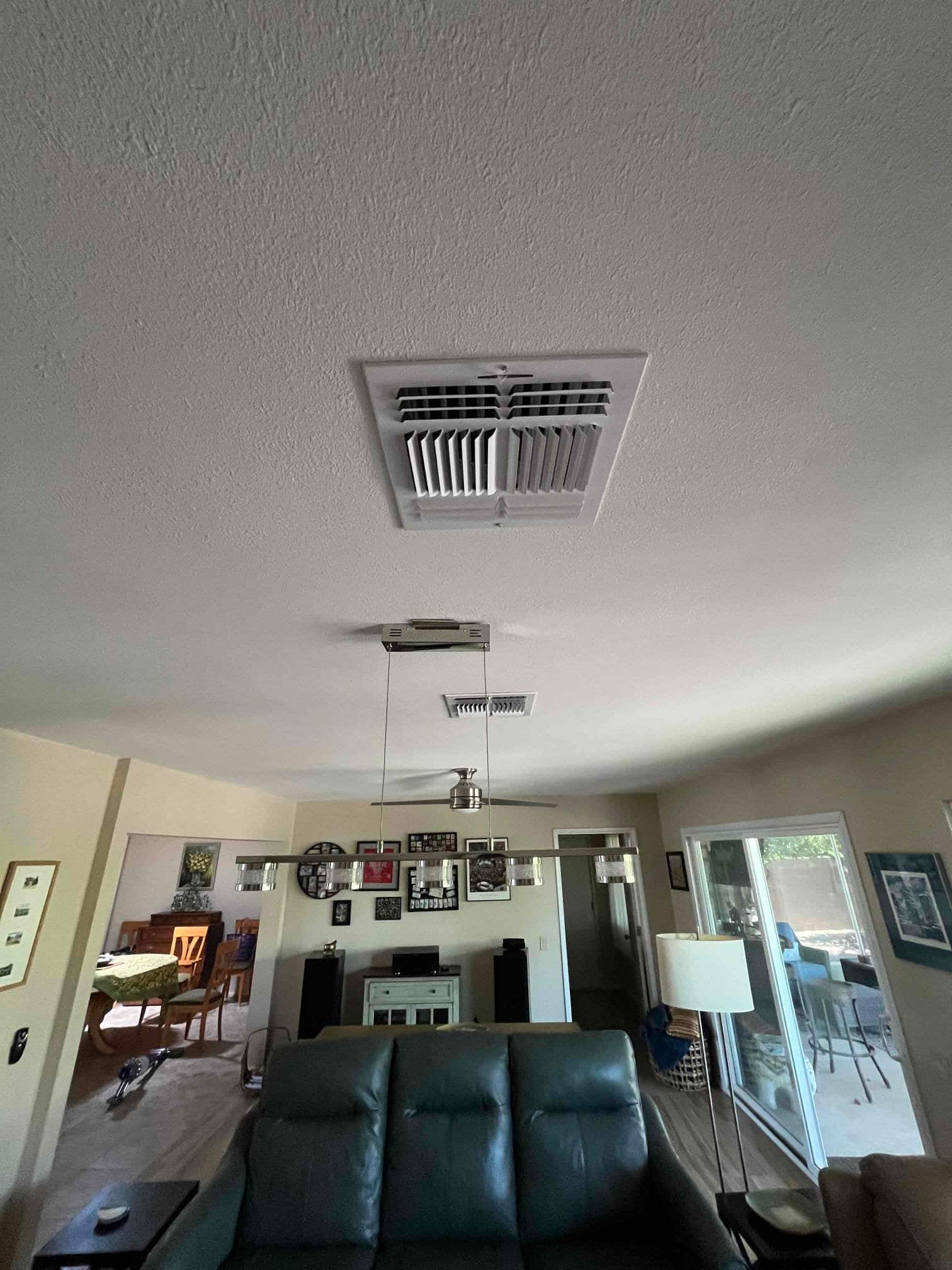 Ceiling supply register installed in the living room, with finished grille centered and surrounding furnishings visible below.