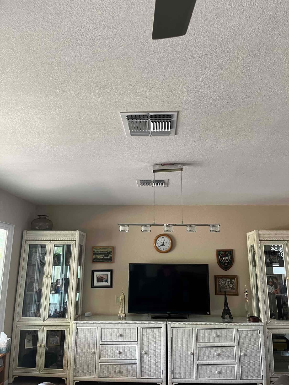 Ceiling supply registers installed and centered in the living room above media cabinets, showing finished air distribution grilles.