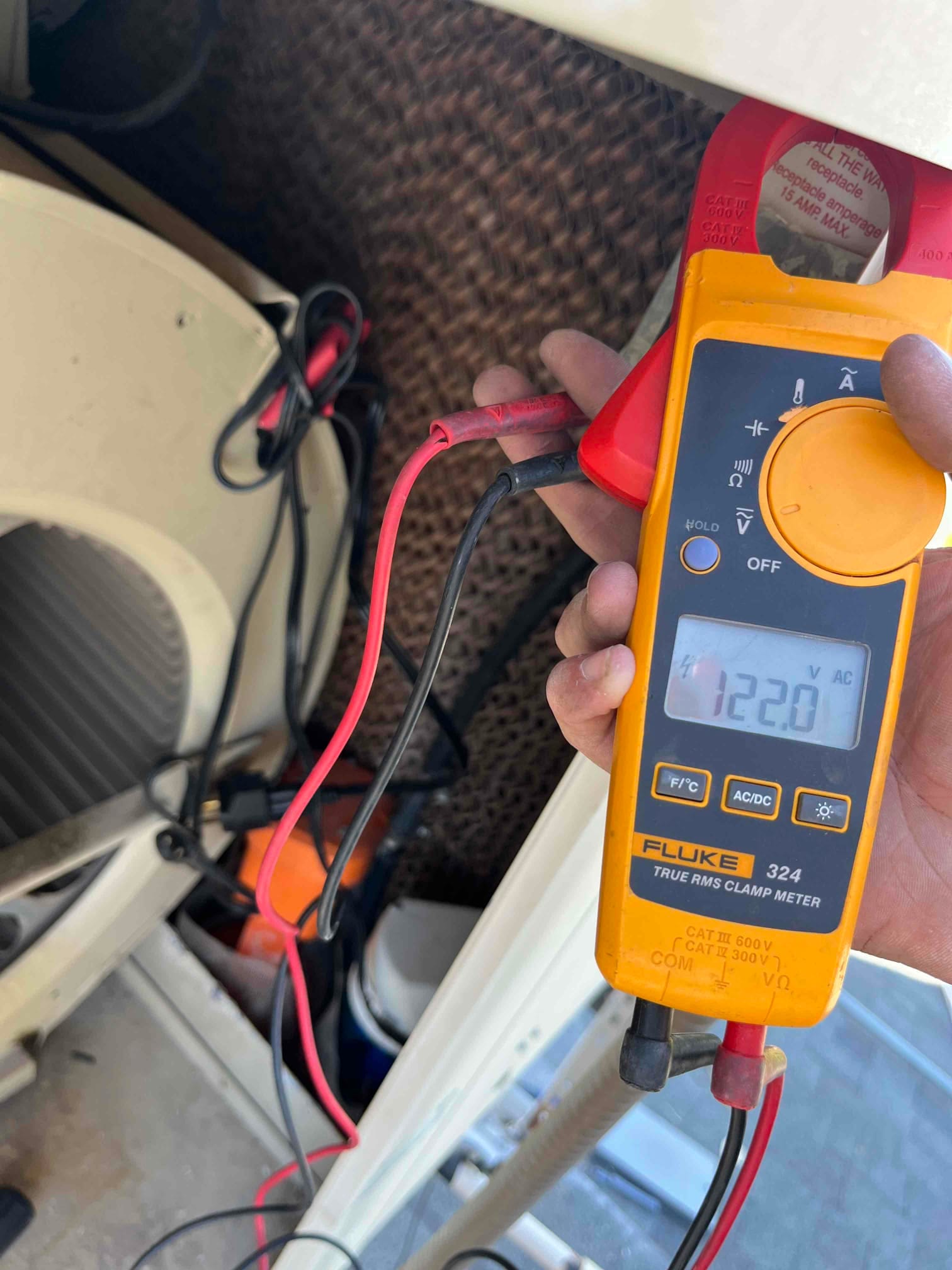 Clamp meter display shows 122.0 V AC while test leads contact an electrical connection inside the cooling equipment cabinet.