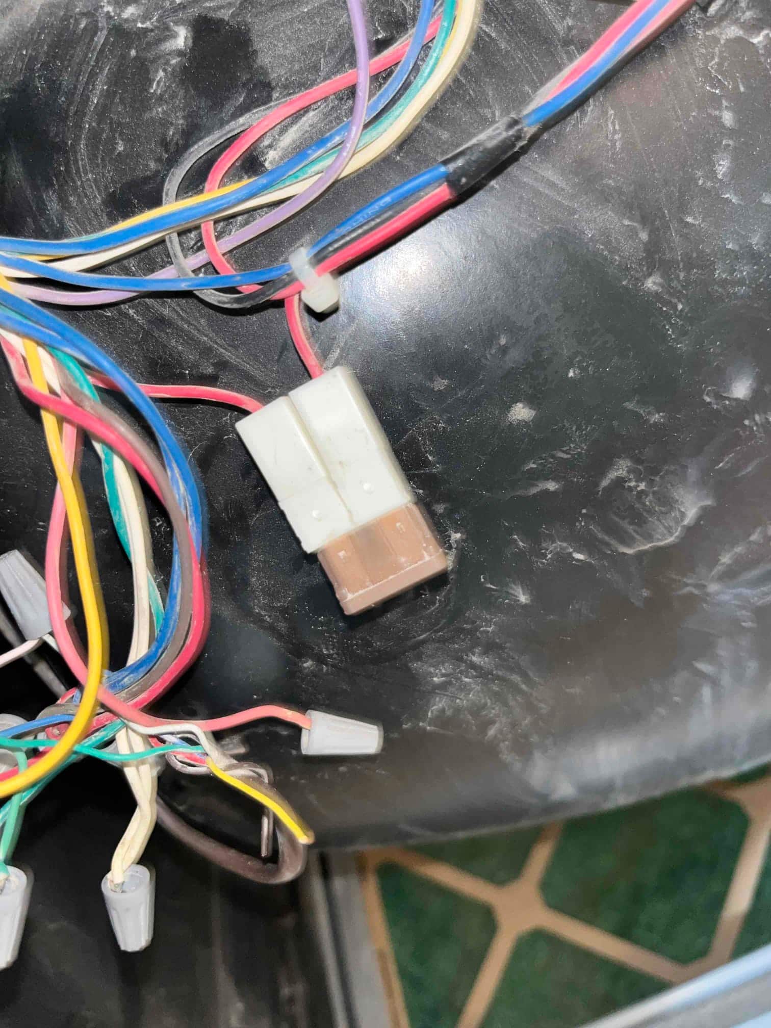 Close-up of furnace wiring harness with multi-pin connector and several color-coded wires secured with wire nuts inside the cabinet.