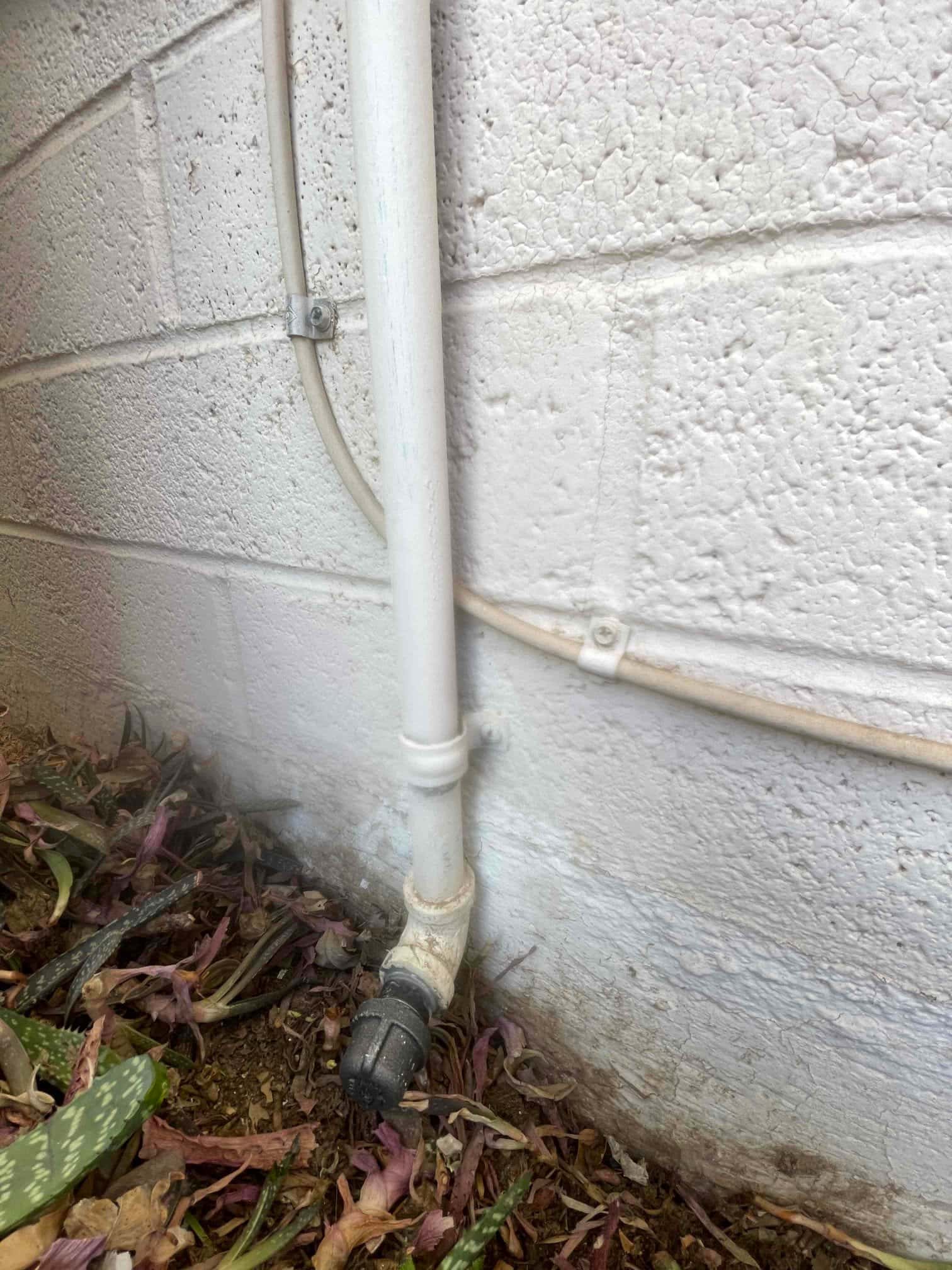 Condensate drain line terminates at exterior wall with cleanout cap and secured control wire alongside the conduit.