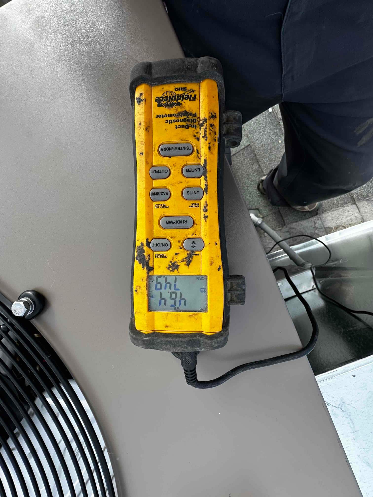 Digital duct thermometer placed on the outdoor unit housing with the display active during air temperature checks.