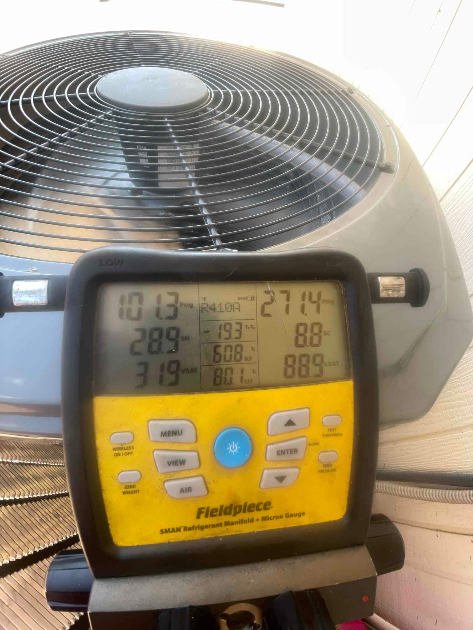 Digital manifold connected at the outdoor unit shows operating suction and liquid pressures with subcooling and superheat readings during system commissioning.