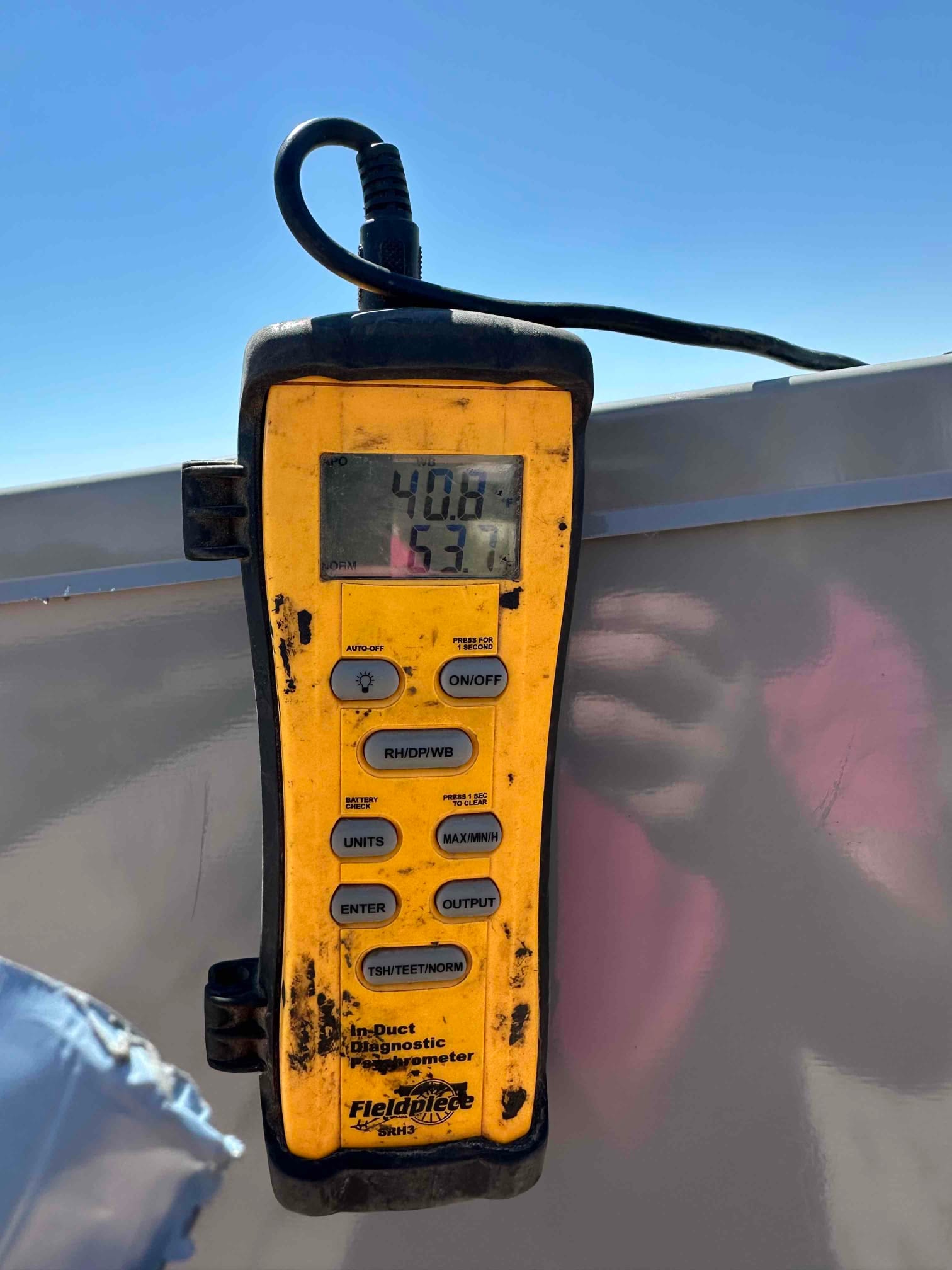 Digital thermometer displays 53.7 degrees Fahrenheit, documenting supply air temperature during commissioning of the mini-split system.