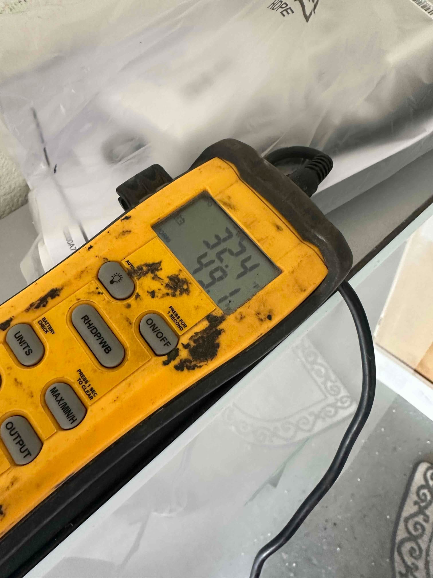Digital thermometer displays air temperatures with a probe connected, documenting readings during HVAC air-side commissioning.