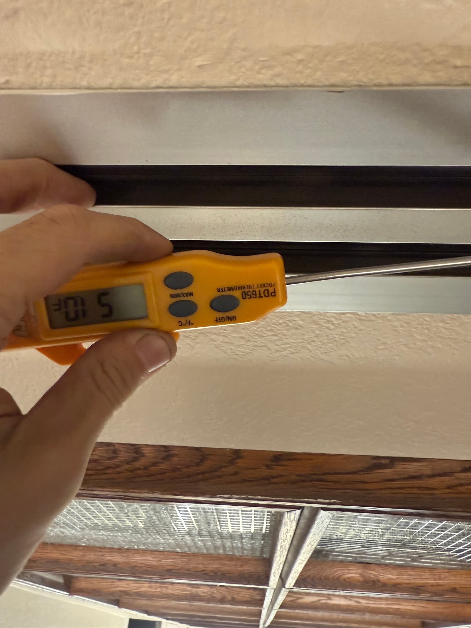 Digital thermometer probe inserted into a ceiling register measures the supply air temperature during system commissioning.