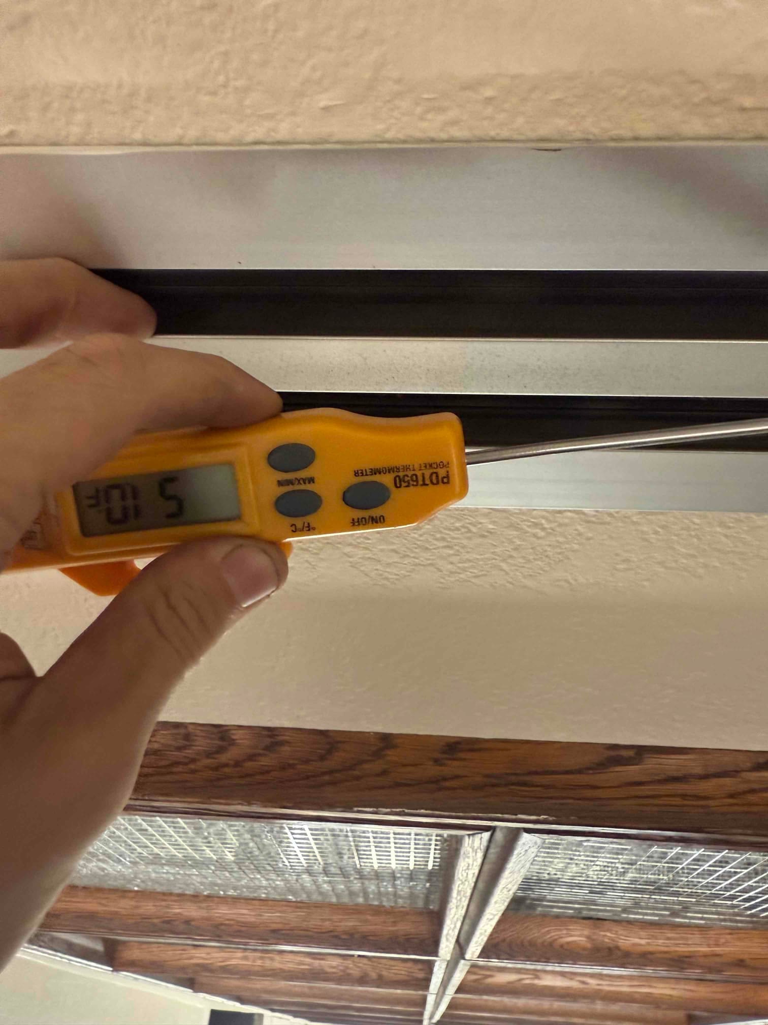 Digital thermometer probe inserted at a ceiling register measures supply air temperature at 51 degrees Fahrenheit during cooling operation.