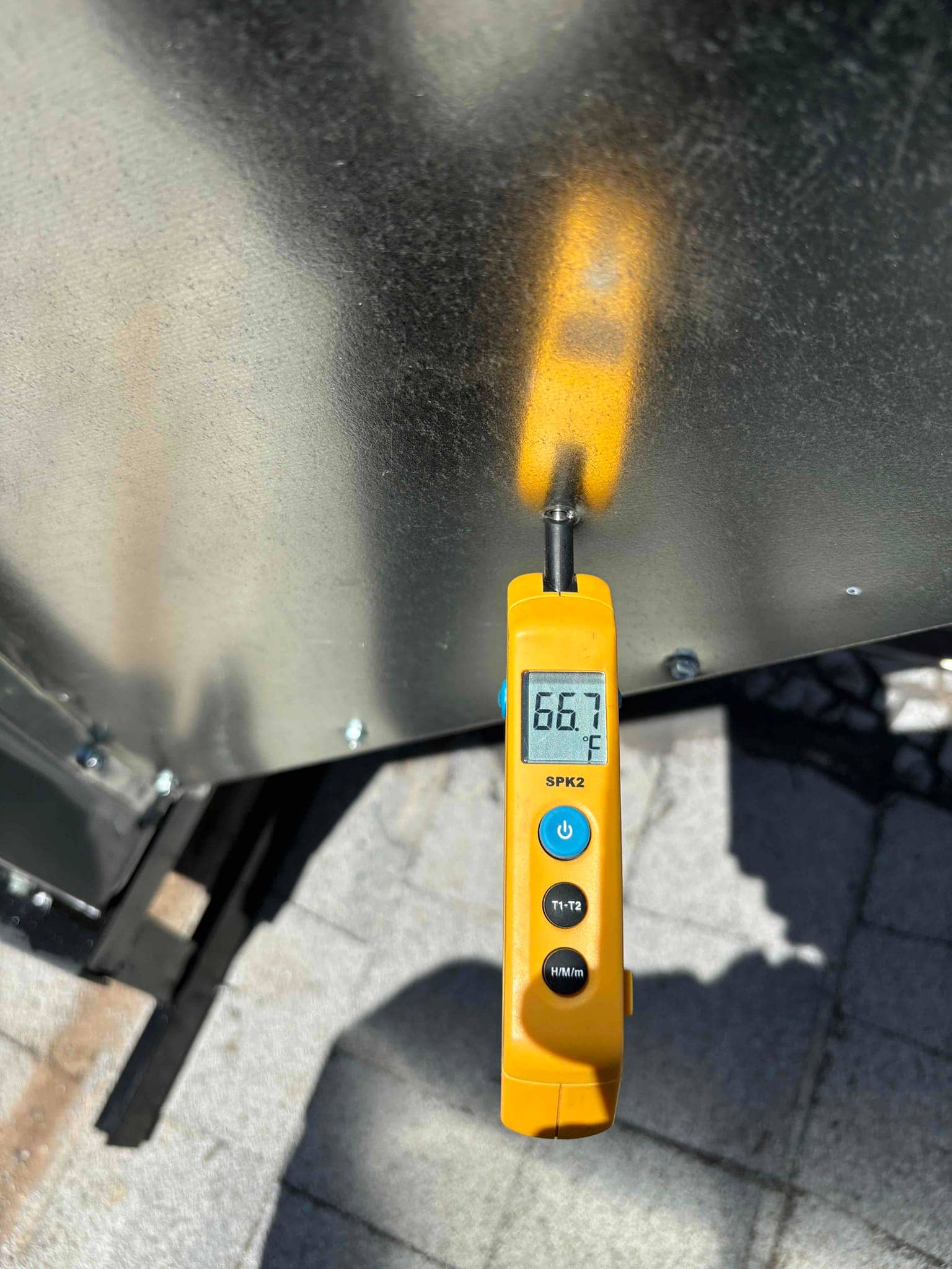 Digital thermometer probe measures air at 66.7 degrees Fahrenheit during HVAC air temperature check near the outdoor unit.