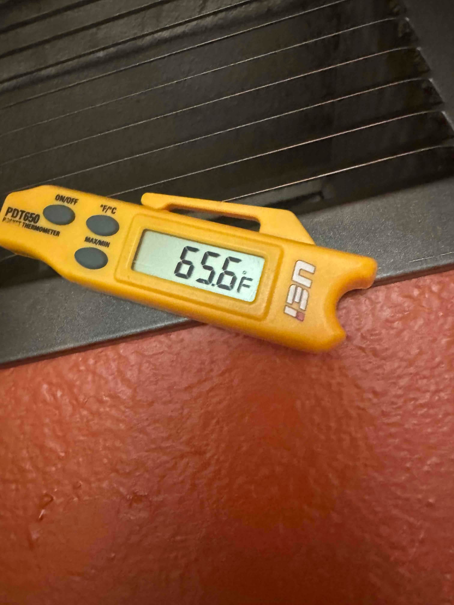 Digital thermometer reads 65.6°F while checking air temperature at a grille during system commissioning.