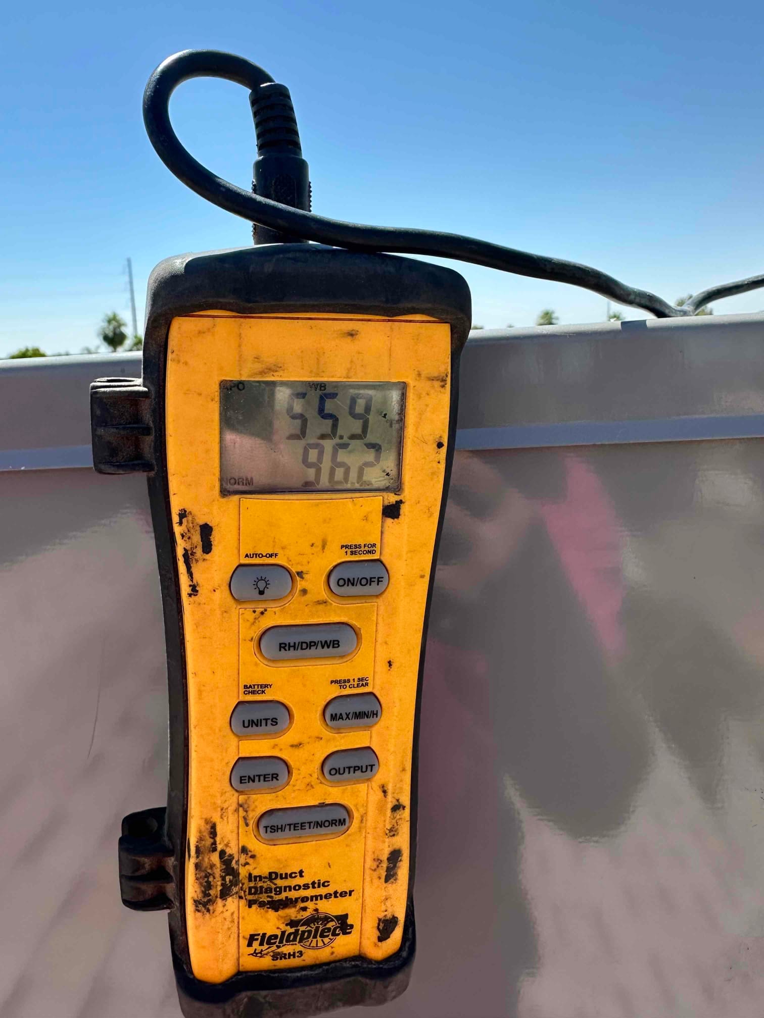 Digital thermometer shows 55.9 degrees Fahrenheit, documenting supply air temperature during mini-split commissioning.