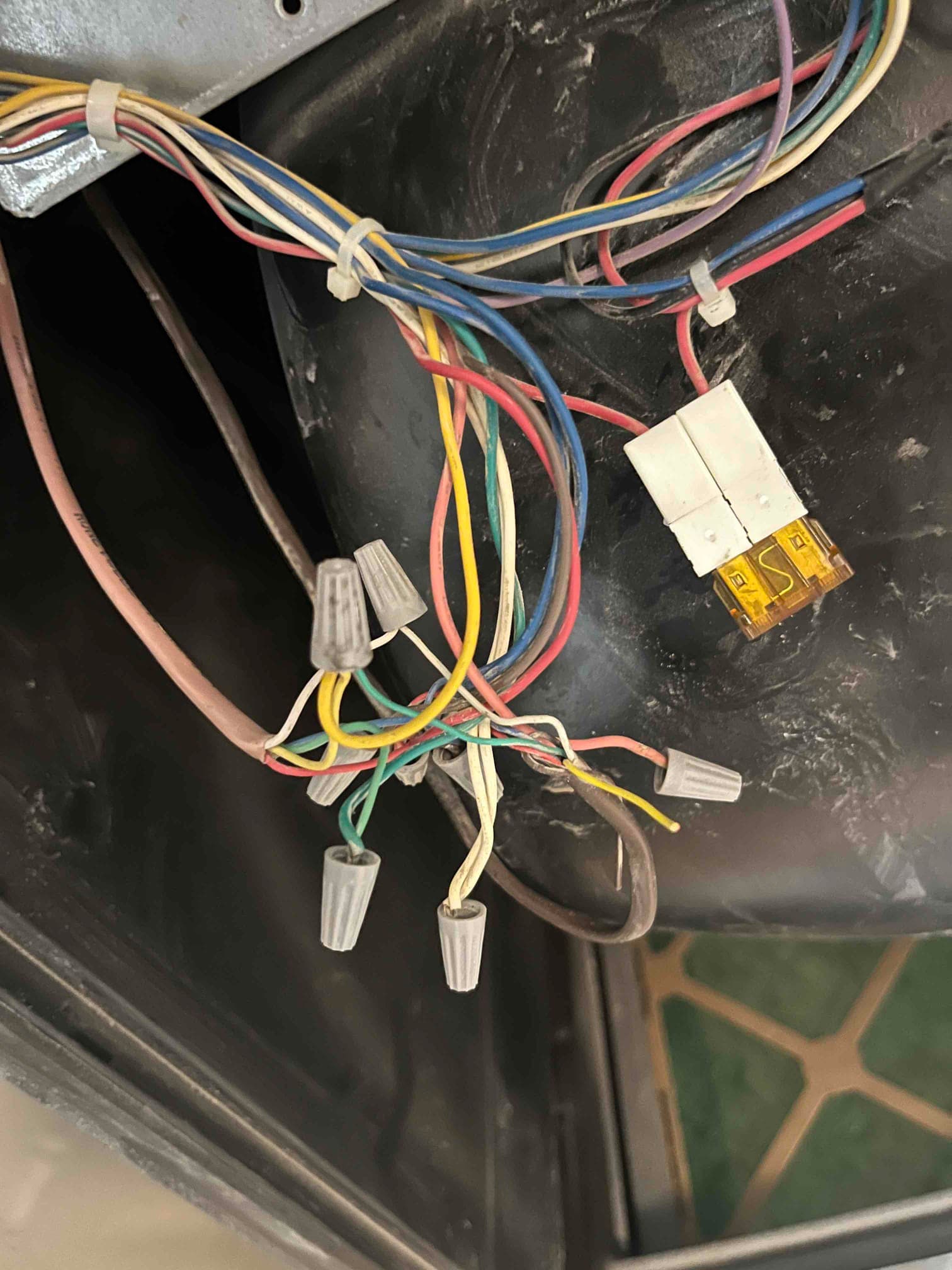 Exposed furnace wiring bundle with multiple wire nuts and dual yellow fuses near the blower compartment.