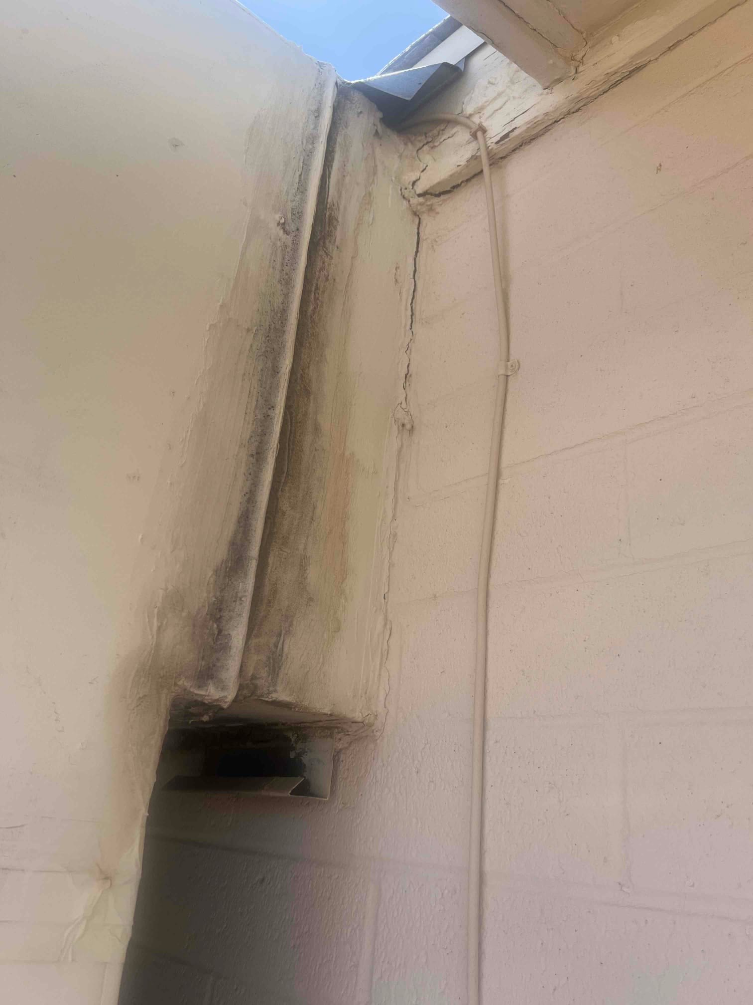 Exterior wall penetration and sealed chase for HVAC lineset, with conduit secured along the block wall near the roof eave.