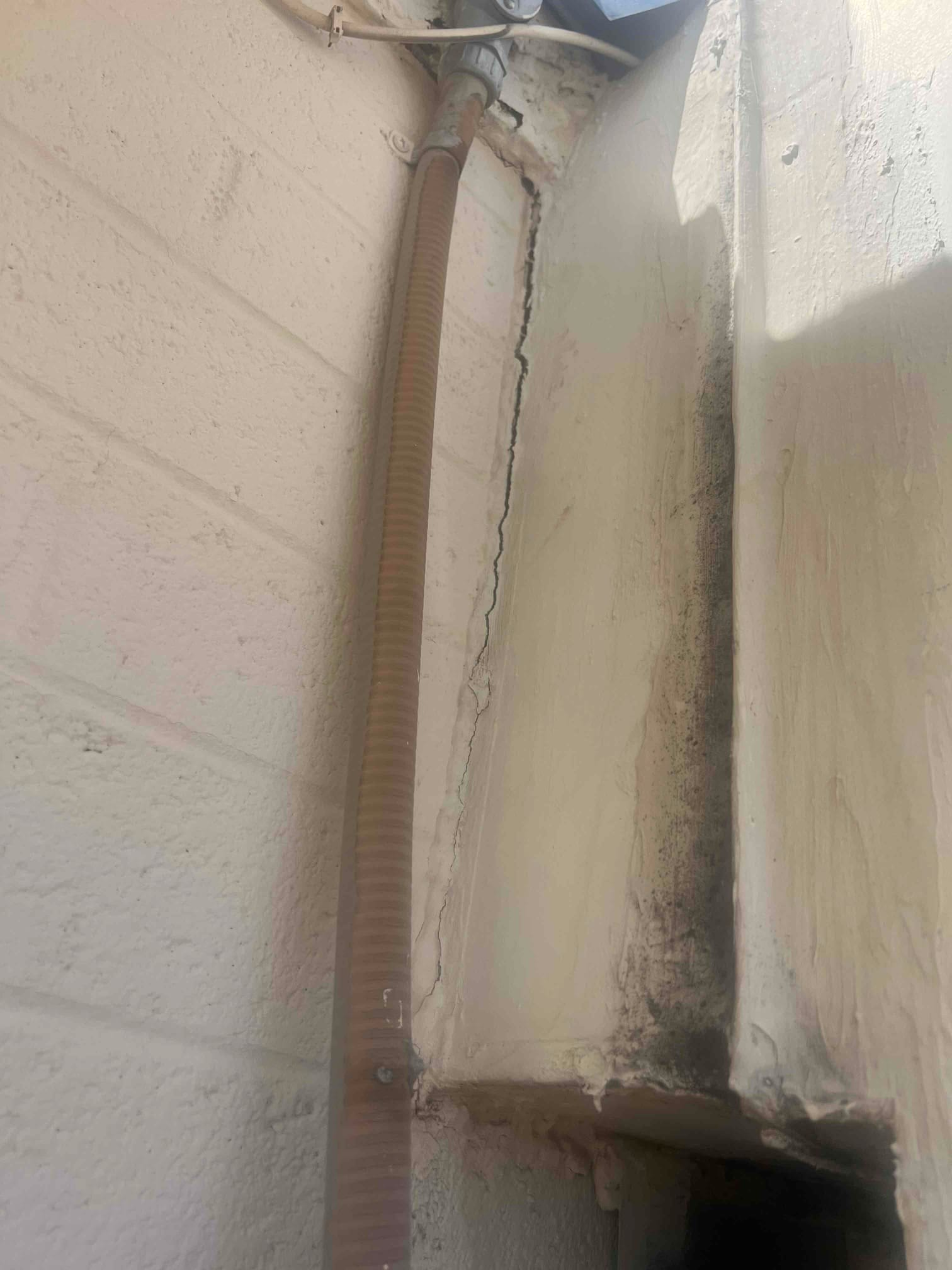 Flexible electrical conduit and sealant at wall penetration beside a stucco chase, showing secured routing along the exterior surface.