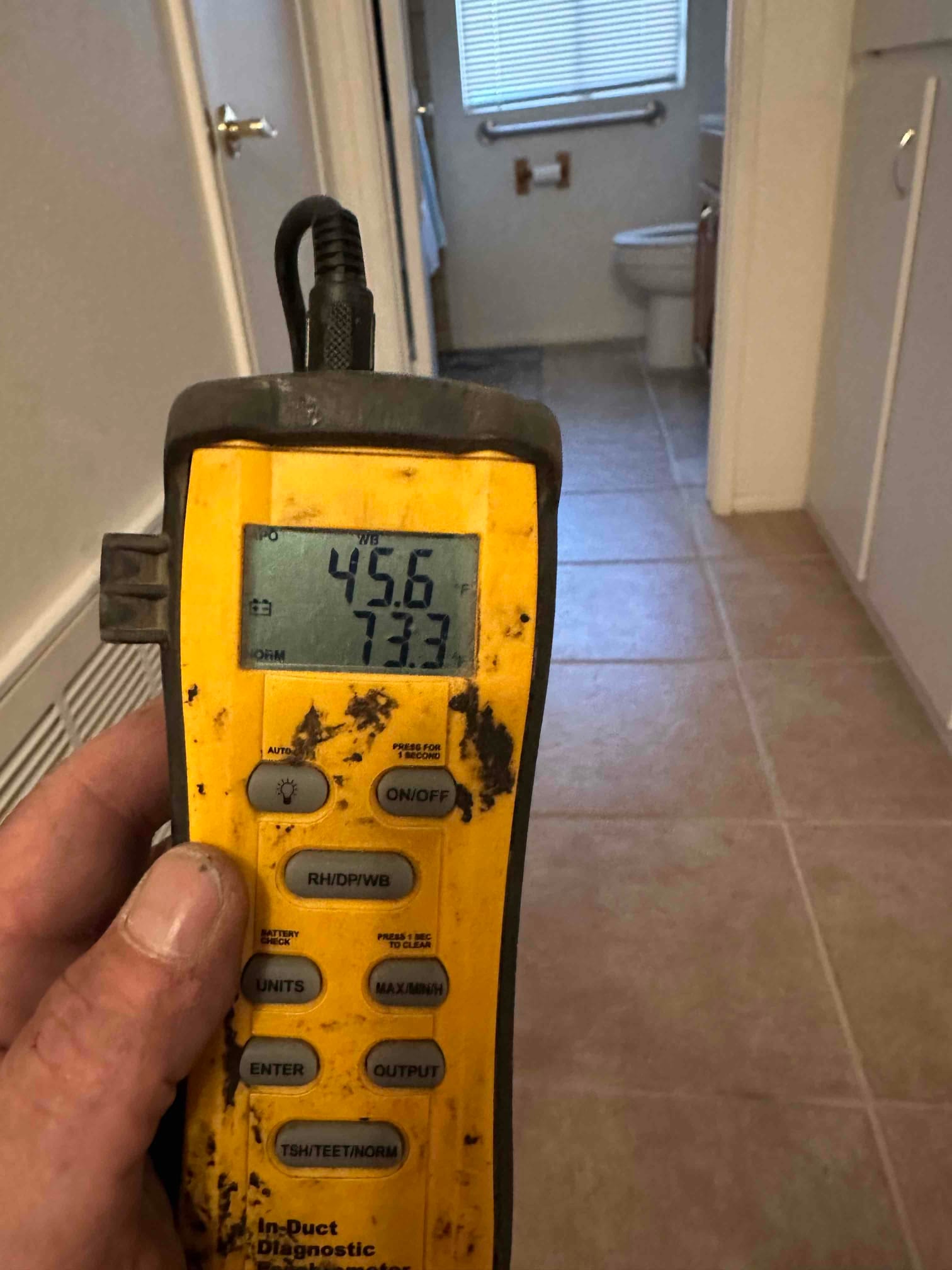 Handheld digital thermometer shows 45.6 degrees Fahrenheit while checking conditioned air at the indoor grille during commissioning.