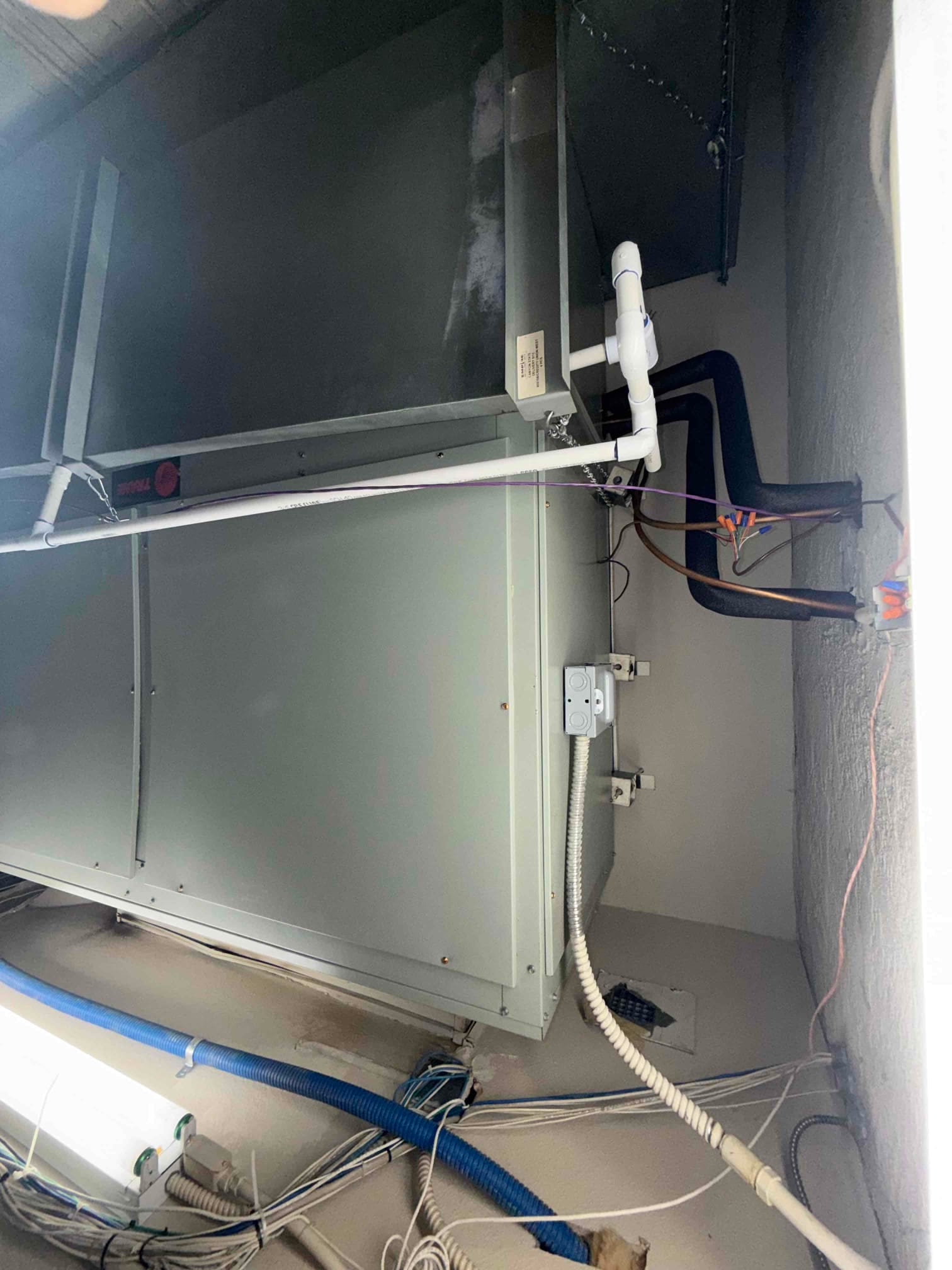 Indoor air handler installed with insulated refrigerant lines, condensate drain with cleanout, and flexible electrical conduit connection.