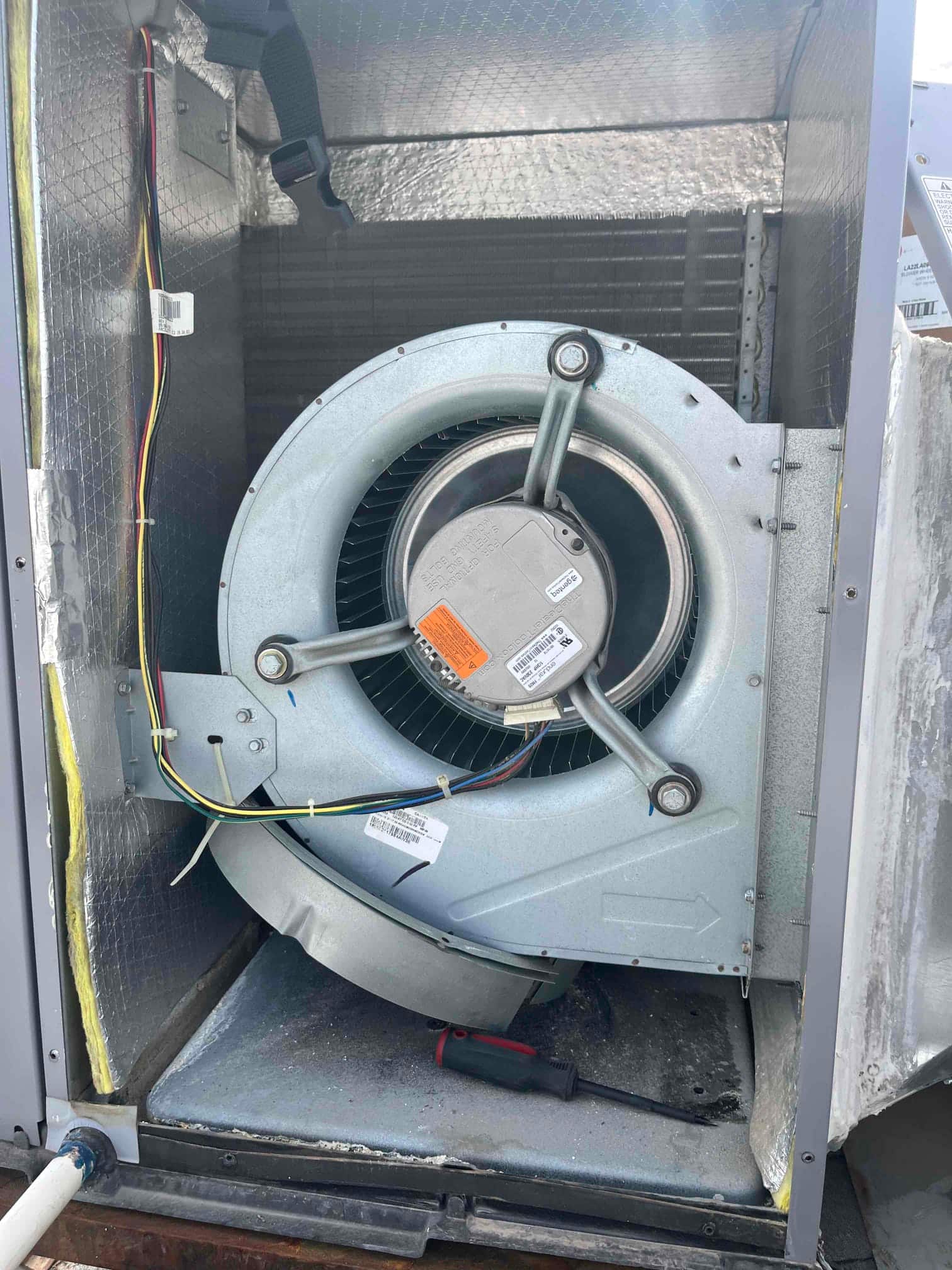 Indoor blower assembly exposed inside the air handler, showing the blower wheel and motor with wiring and mounting brackets.