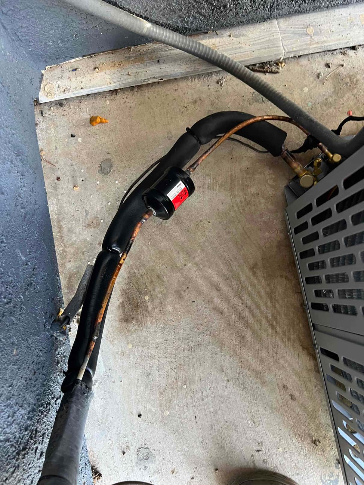 Insulated refrigerant line set with suction accumulator and filter-drier connected to the outdoor condenser on a concrete pad.
