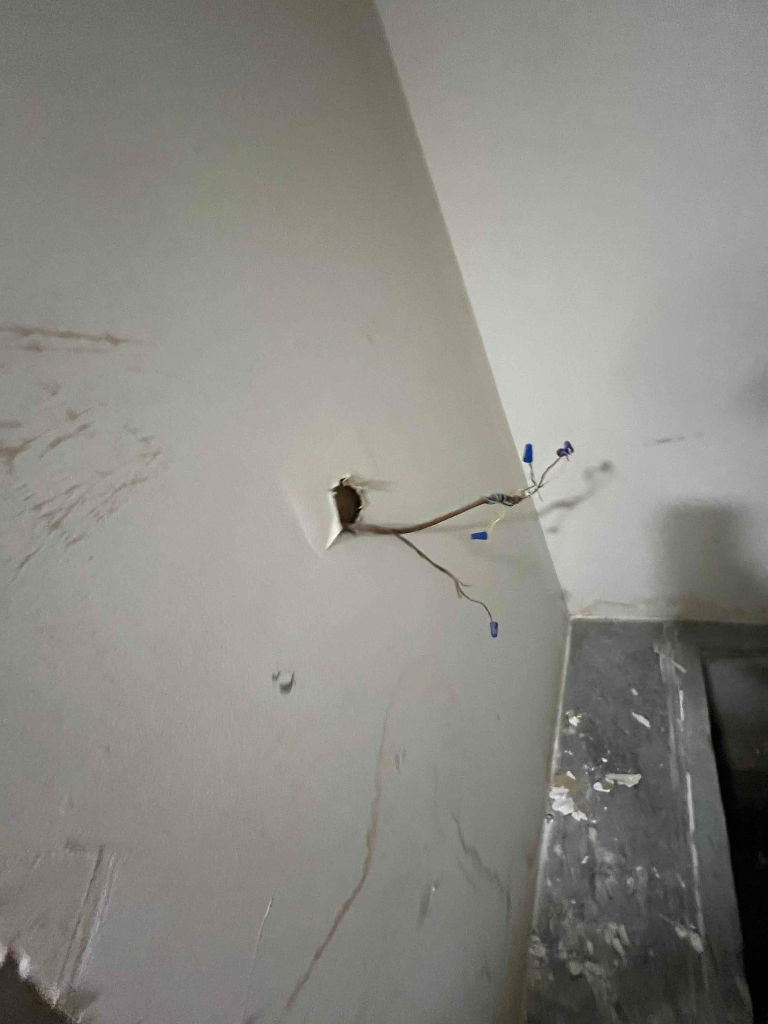 Low-voltage thermostat wires emerge from a wall opening with wire connectors during HVAC installation rough-in.