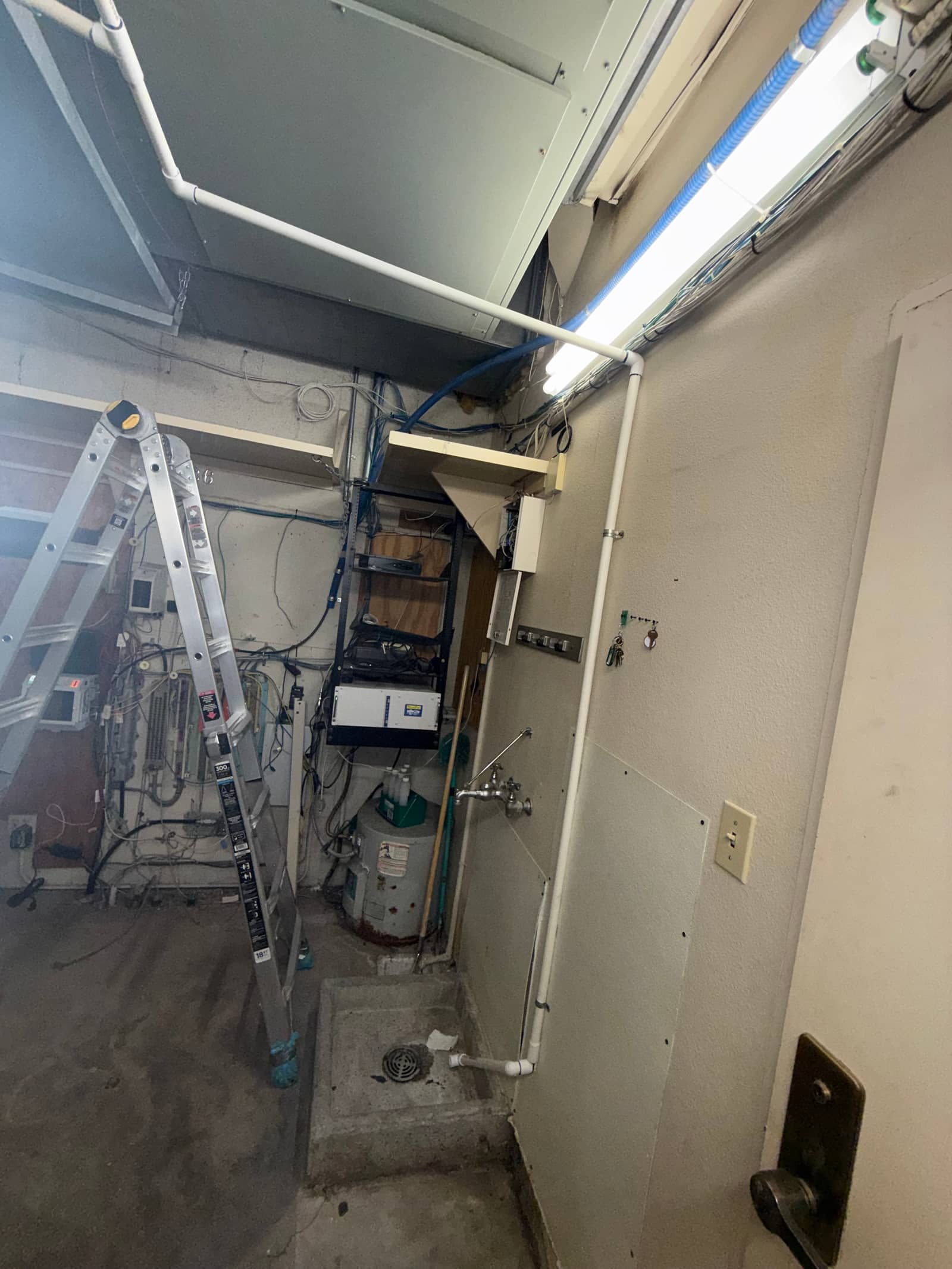 Mechanical room showing new condensate drain piping, suspended ductwork, and workspace with ladder and service drain.