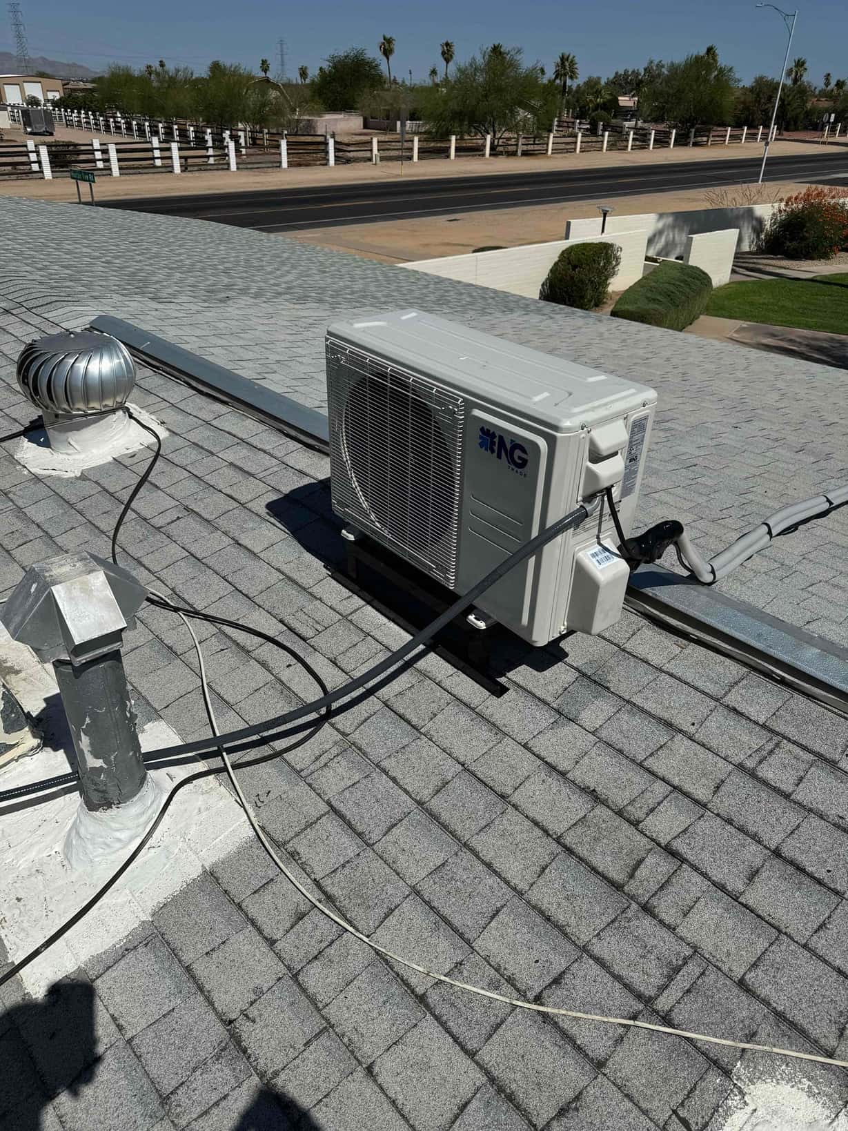 Mini-split outdoor condenser mounted on rooftop rails with insulated line set and electrical whip routed along a metal channel.