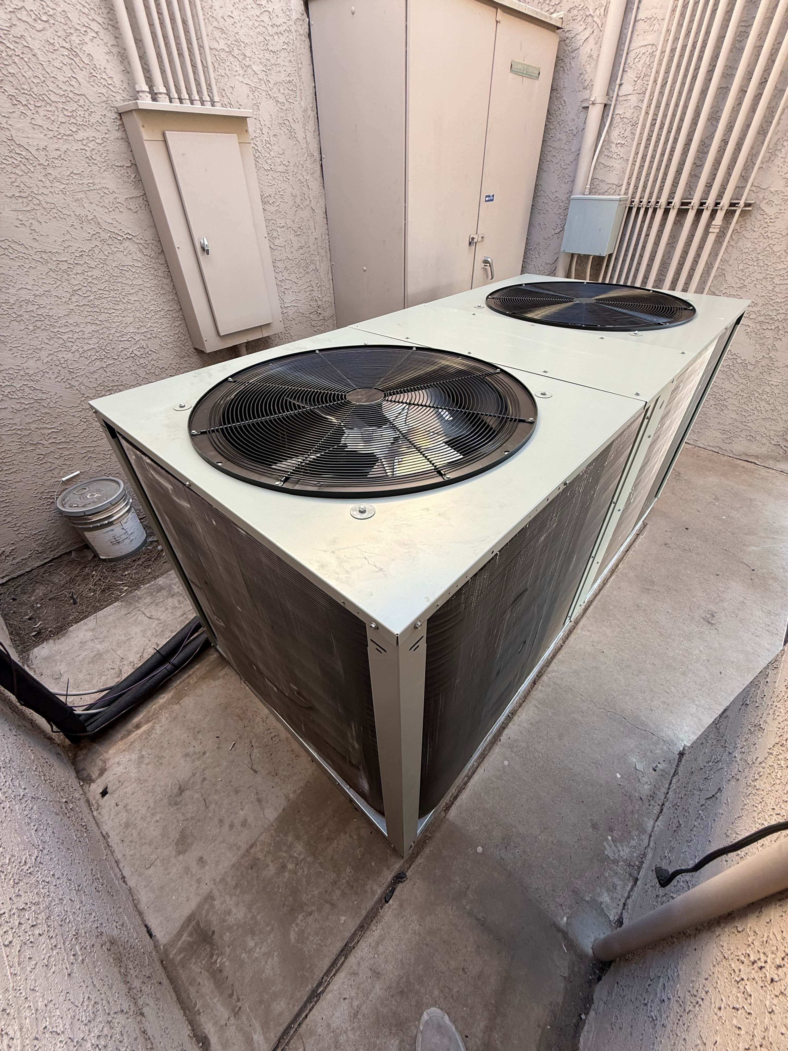 New dual-fan outdoor heat pump condenser set on a level pad with insulated refrigerant lines routed along the wall.