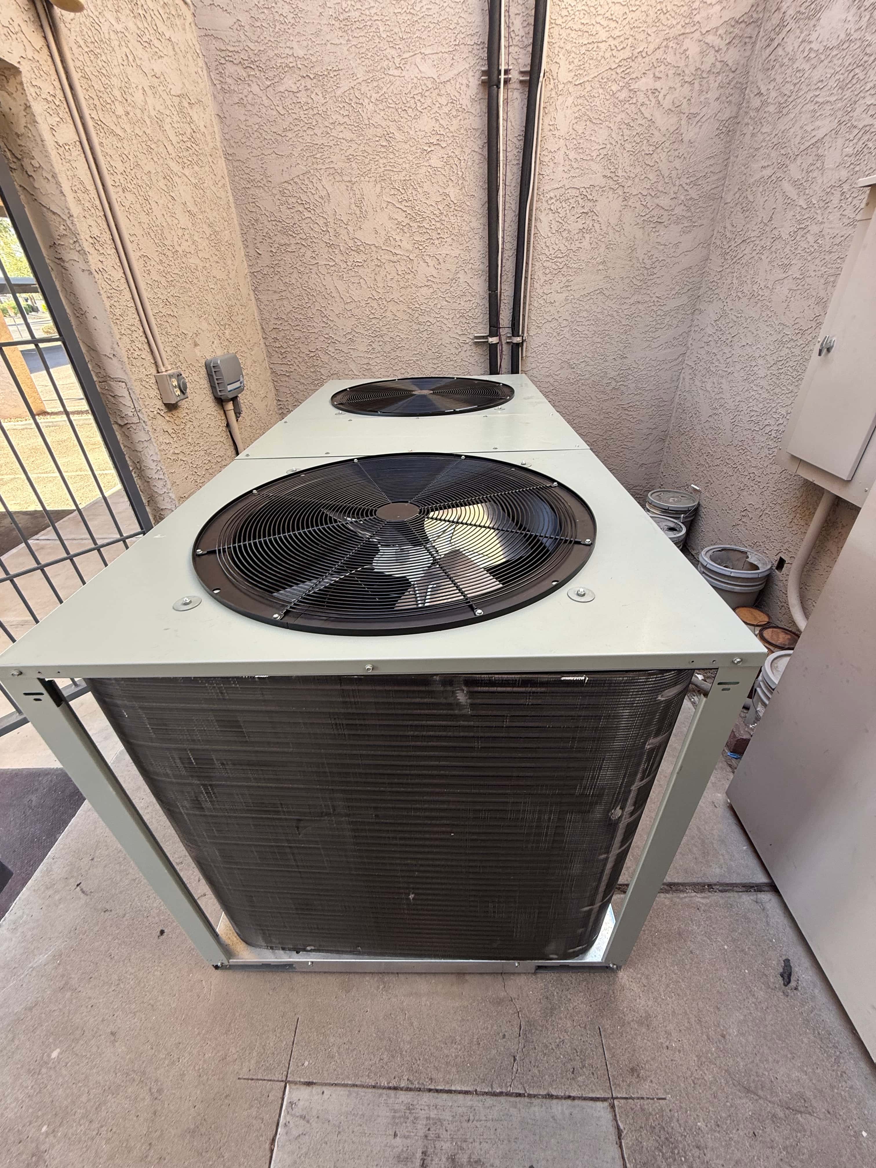New dual-fan outdoor heat pump condenser set in a walled service area with electrical conduit and secured refrigerant line penetrations.