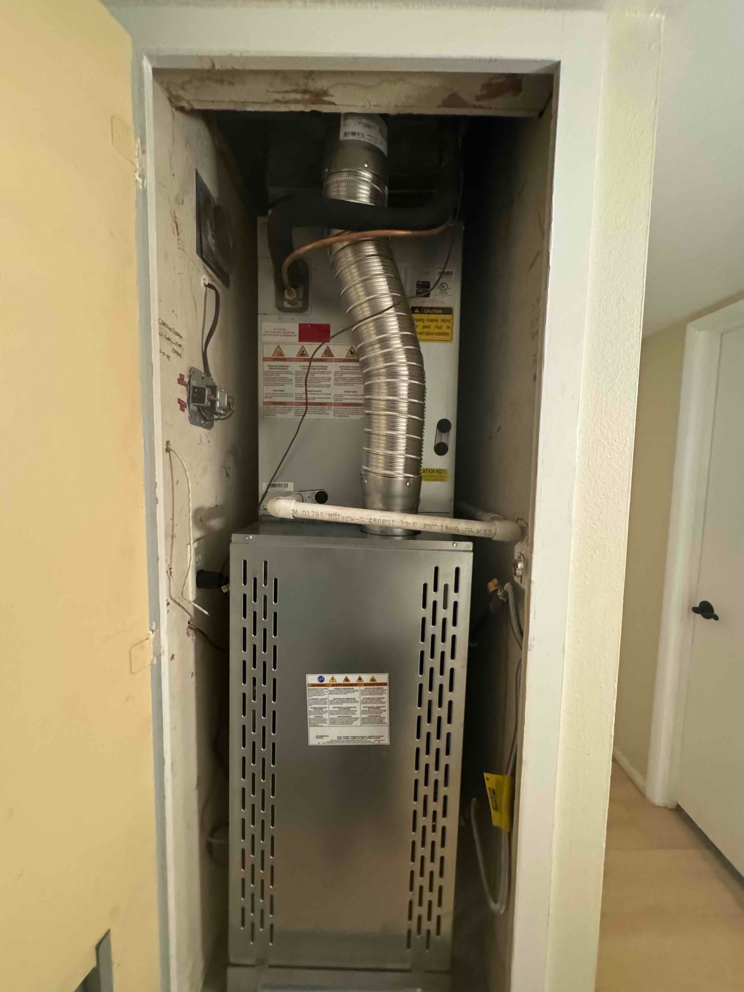 New gas furnace installed in a closet with flue vent, condensate drain piping, and refrigerant line connections visible.