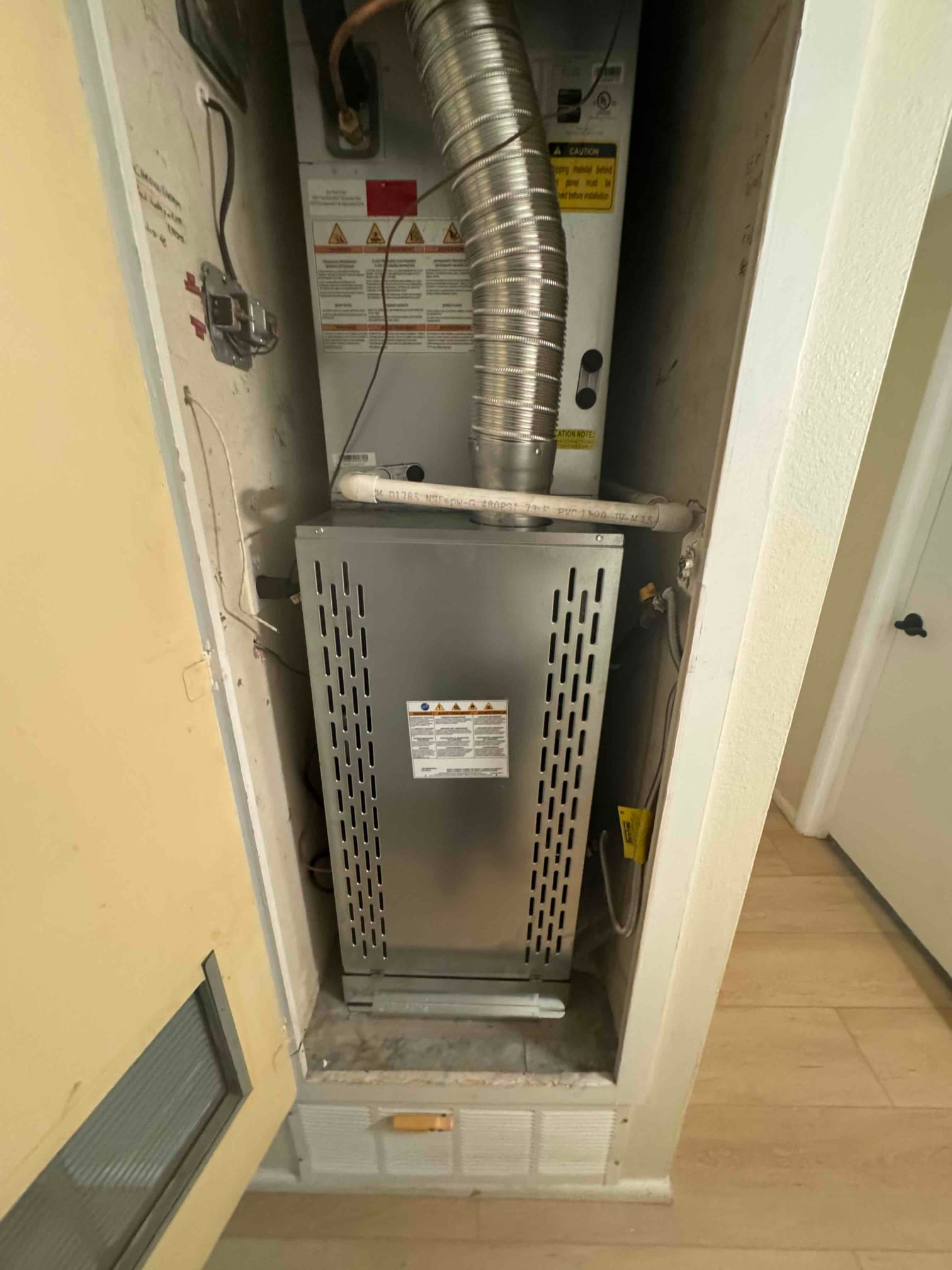 New gas furnace installed in a closet with vent connector, condensate drain, and return grille below the cabinet.