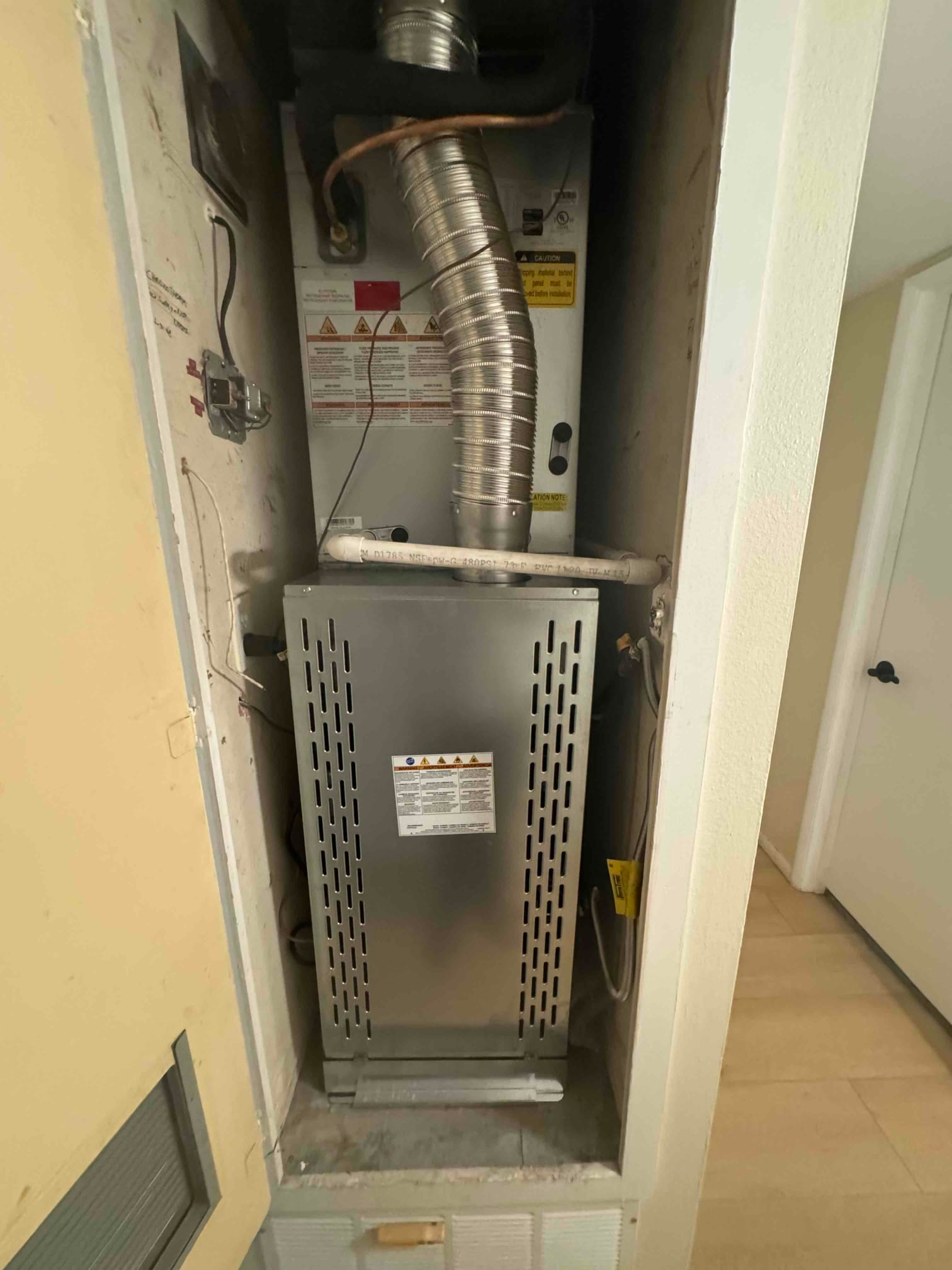 New gas furnace installed in a closet with vent connector, drain line, and service disconnect visible on the side wall.