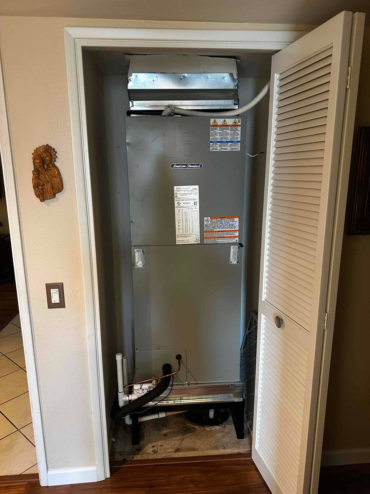 New indoor air handler installed in a closet with insulated drain piping, filter slot, and transition ductwork at the top.