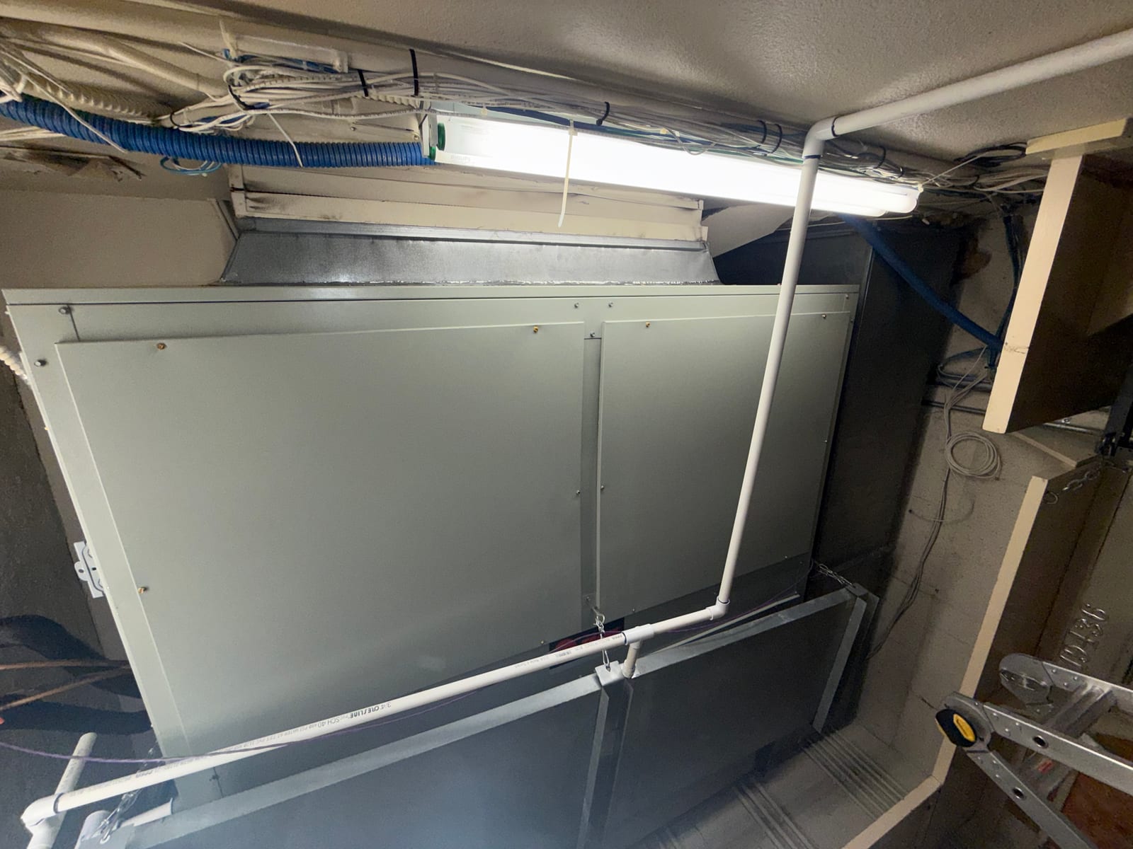 New indoor air handler installed with sealed duct transitions, supported by hangers, and PVC condensate drain routed alongside the cabinet.
