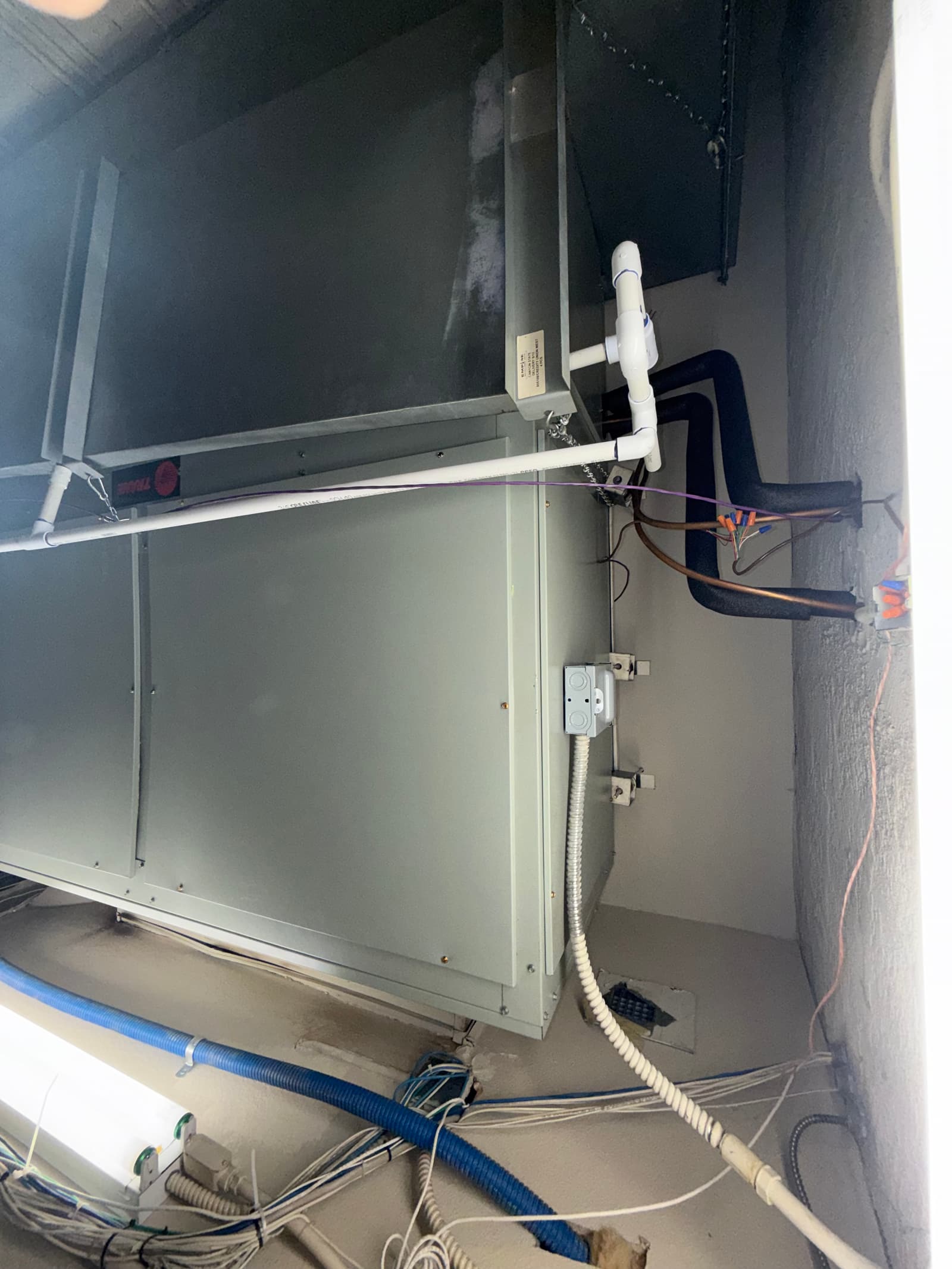 New indoor air handler set with insulated refrigerant lines, condensate drain with cleanout, electrical whip, and connected duct transitions.