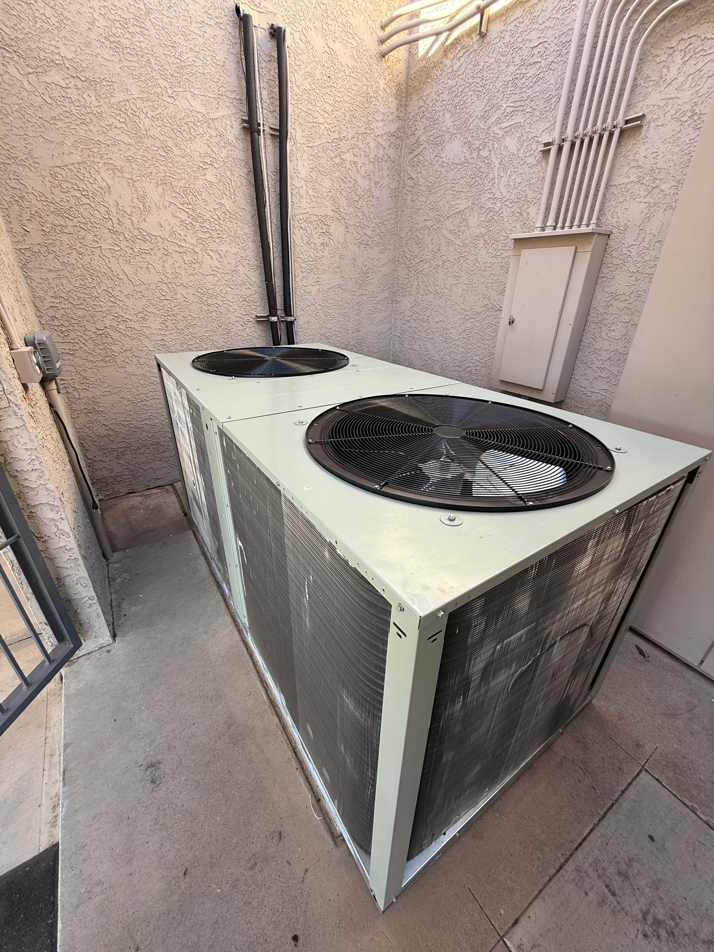 Two new outdoor condenser units set on a level pad with insulated line sets routed up the wall to electrical service.