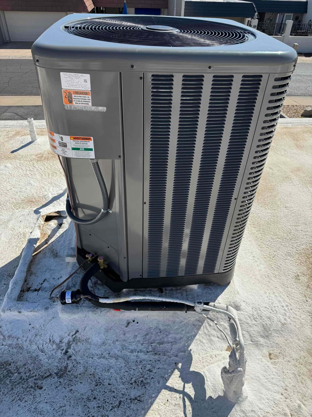 New outdoor heat pump condenser set on a coated rooftop with insulated refrigerant lines and electrical whip connected.