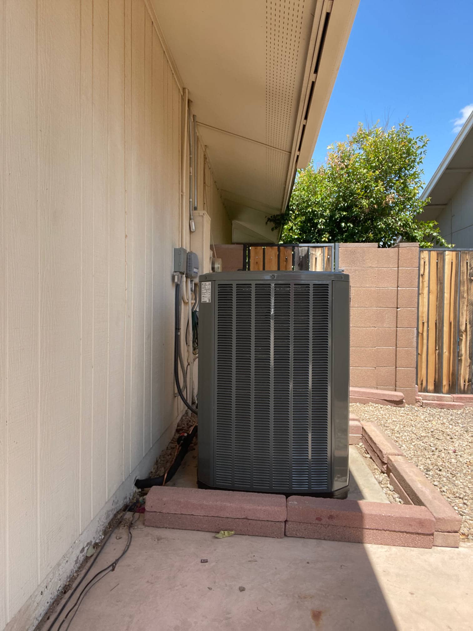New outdoor heat pump condenser set on a level pad with connected electrical whip and insulated refrigerant line set.