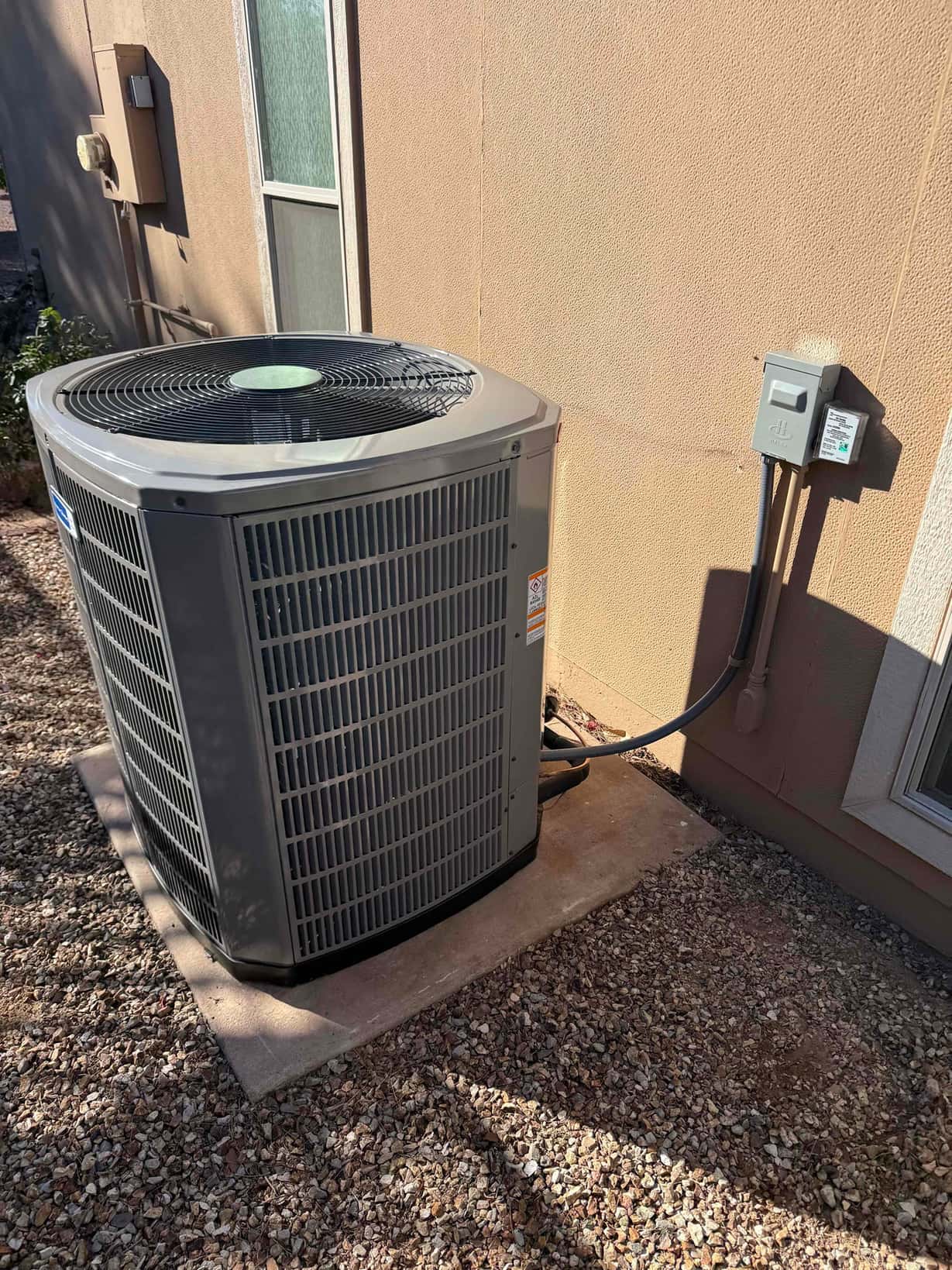 New outdoor heat pump condenser set on a level pad with insulated line set and weatherproof electrical disconnect installed.