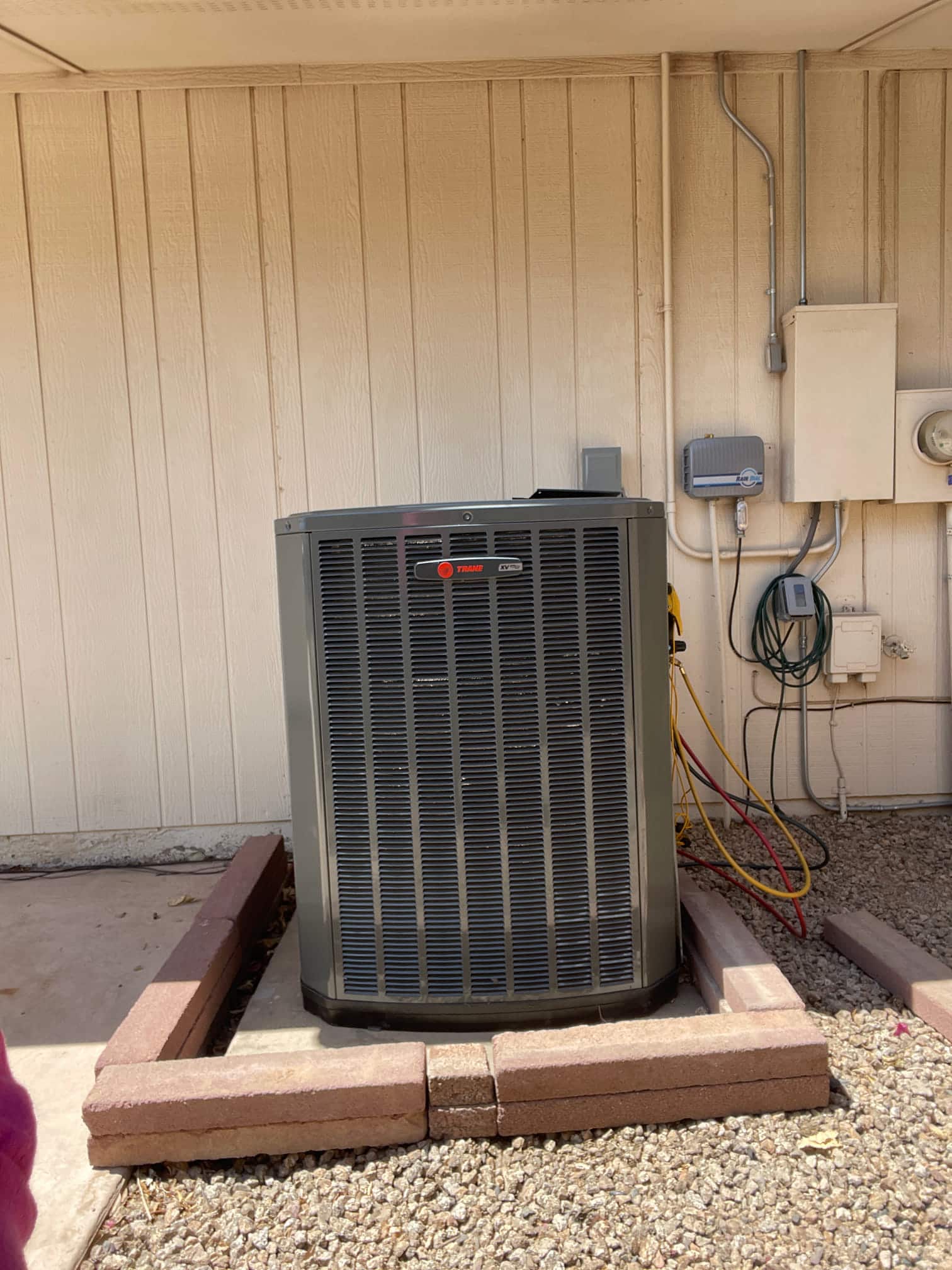 New outdoor heat pump condenser set on a level pad with refrigerant hoses connected and electrical disconnect mounted nearby.